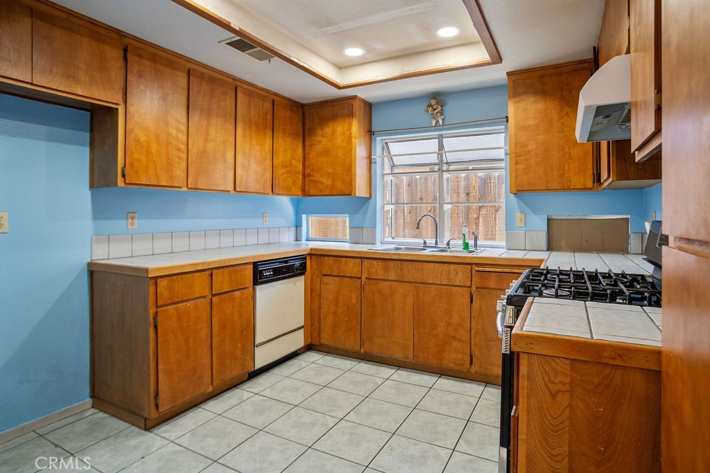 Kitchen with wood cabinets, blue walls, tiled counters and floor, and a window over the sink.