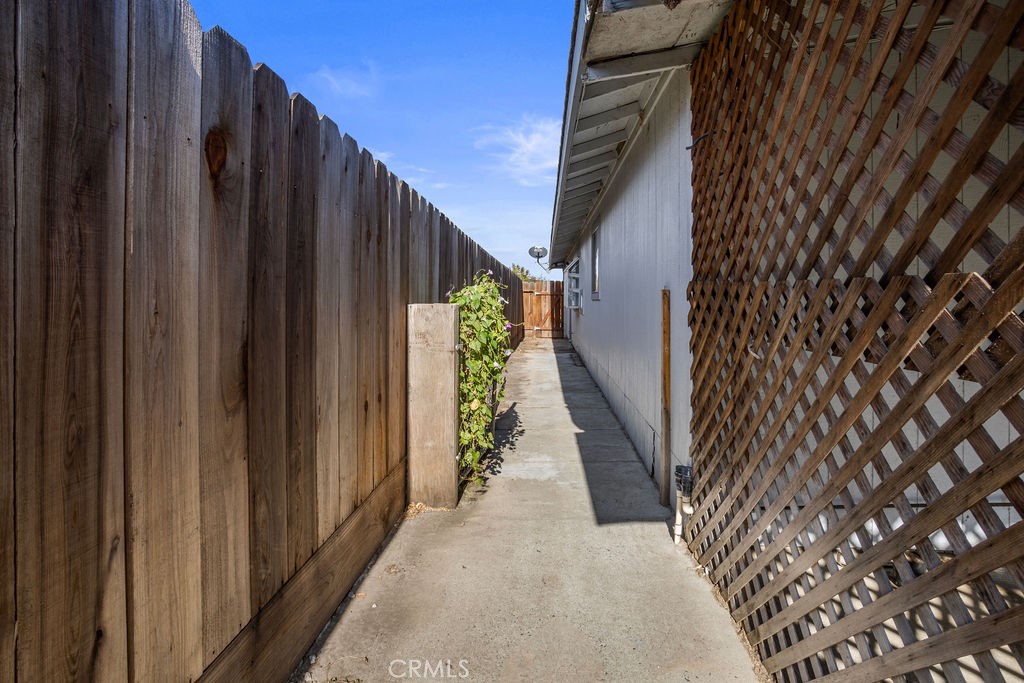Side walkway beside the house, bordered by a tall wooden fence and lattice-covered wall.