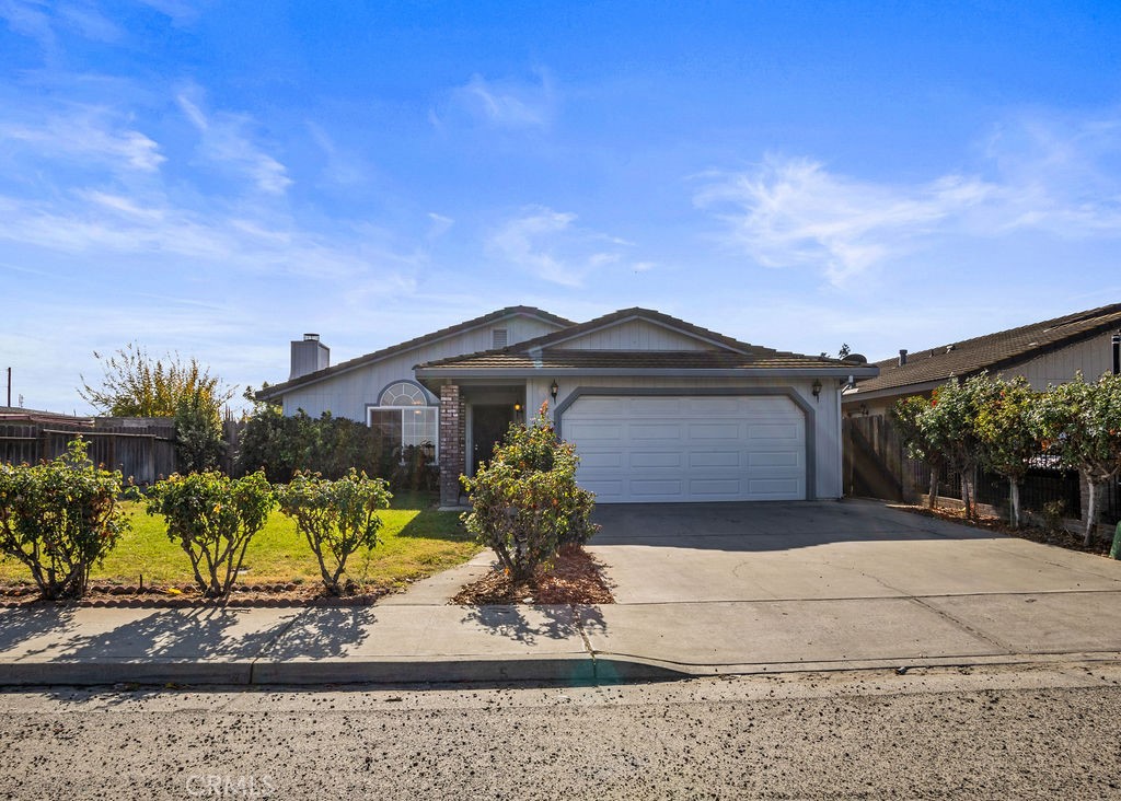 Single-story house with a double garage, broad driveway, and shrubs across the front lawn.