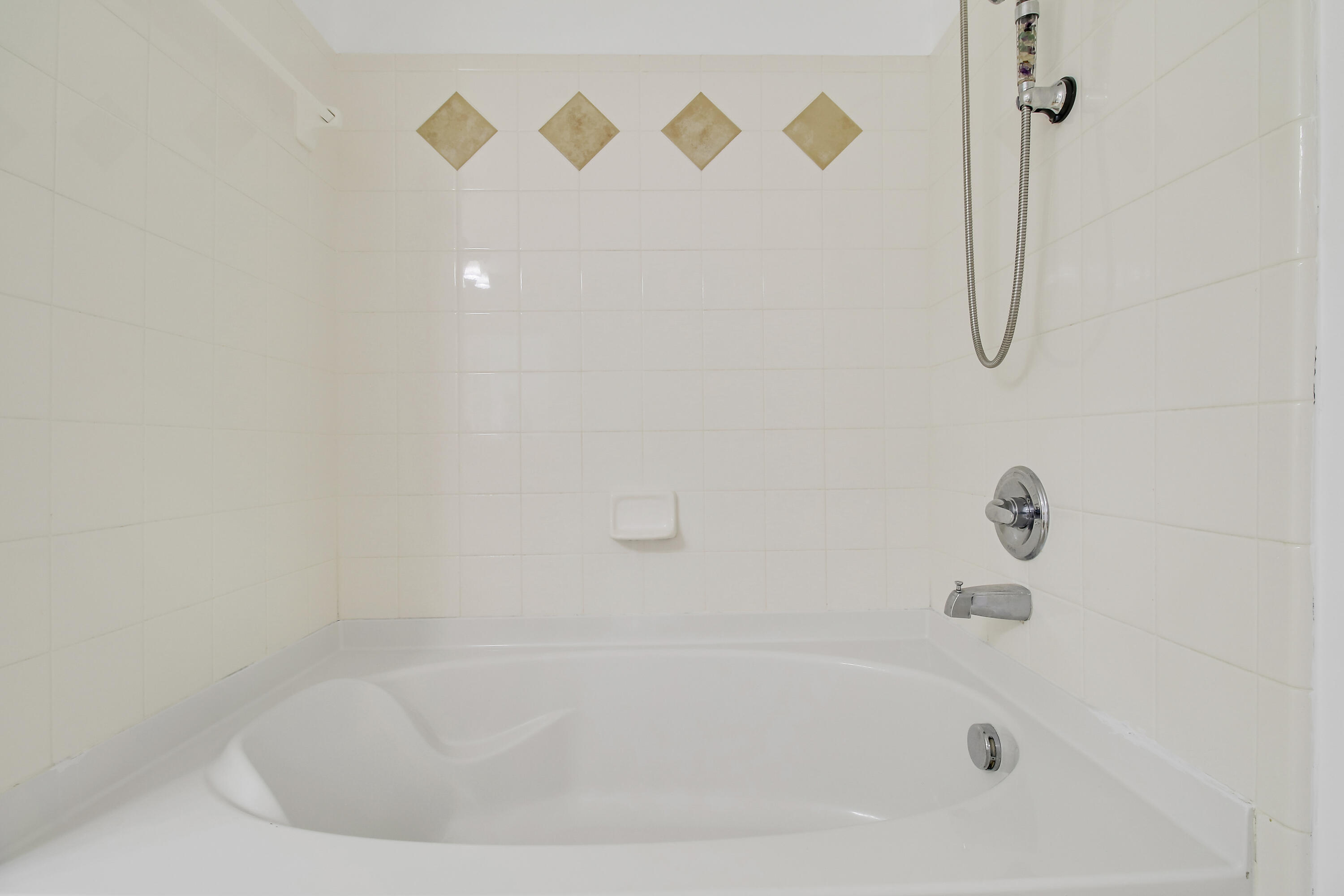 White bathtub and shower with chrome fixtures and tan diamond accent tiles.