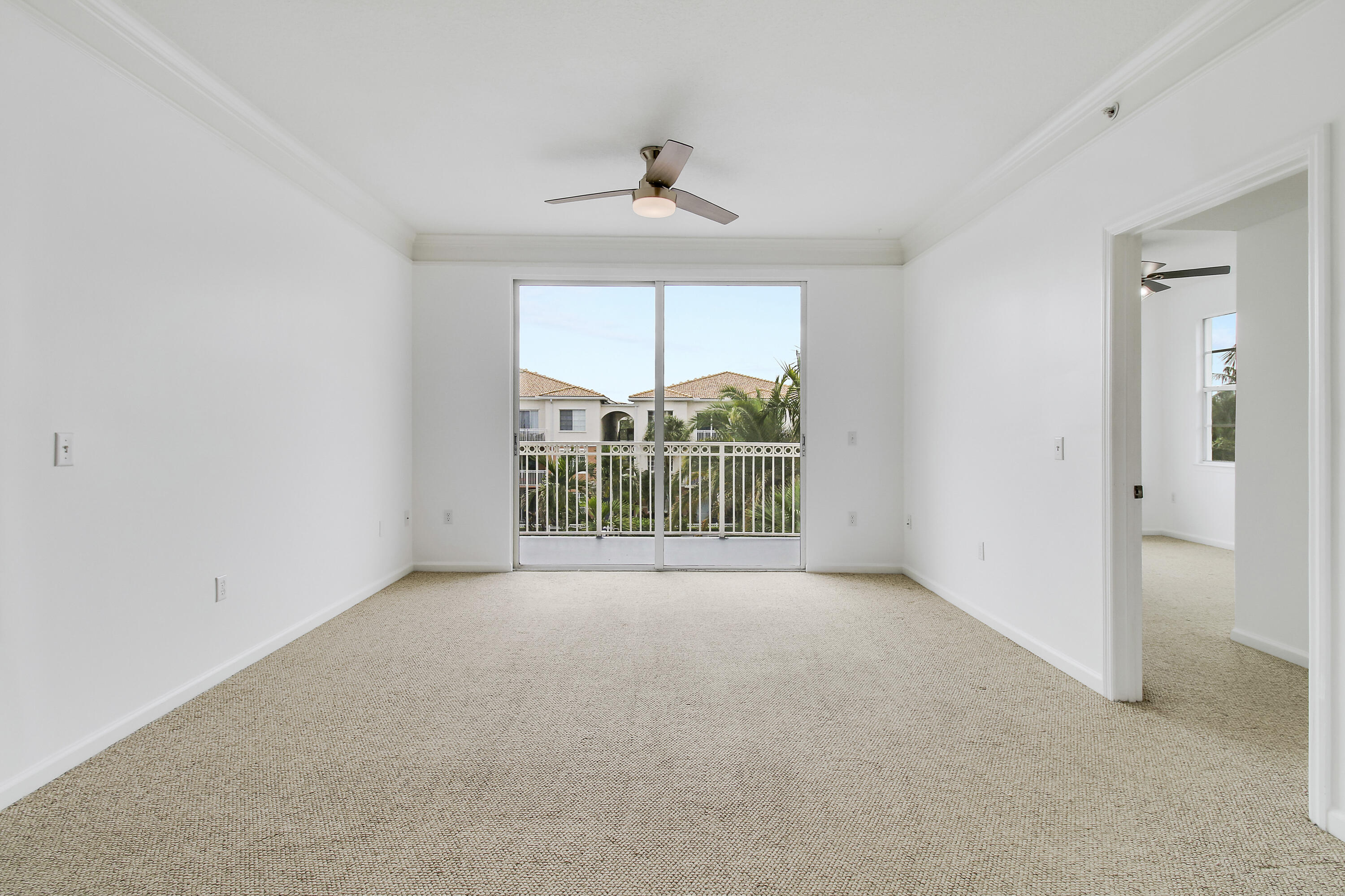Vacant carpeted bedroom with a ceiling fan and sliding doors opening to a balcony.