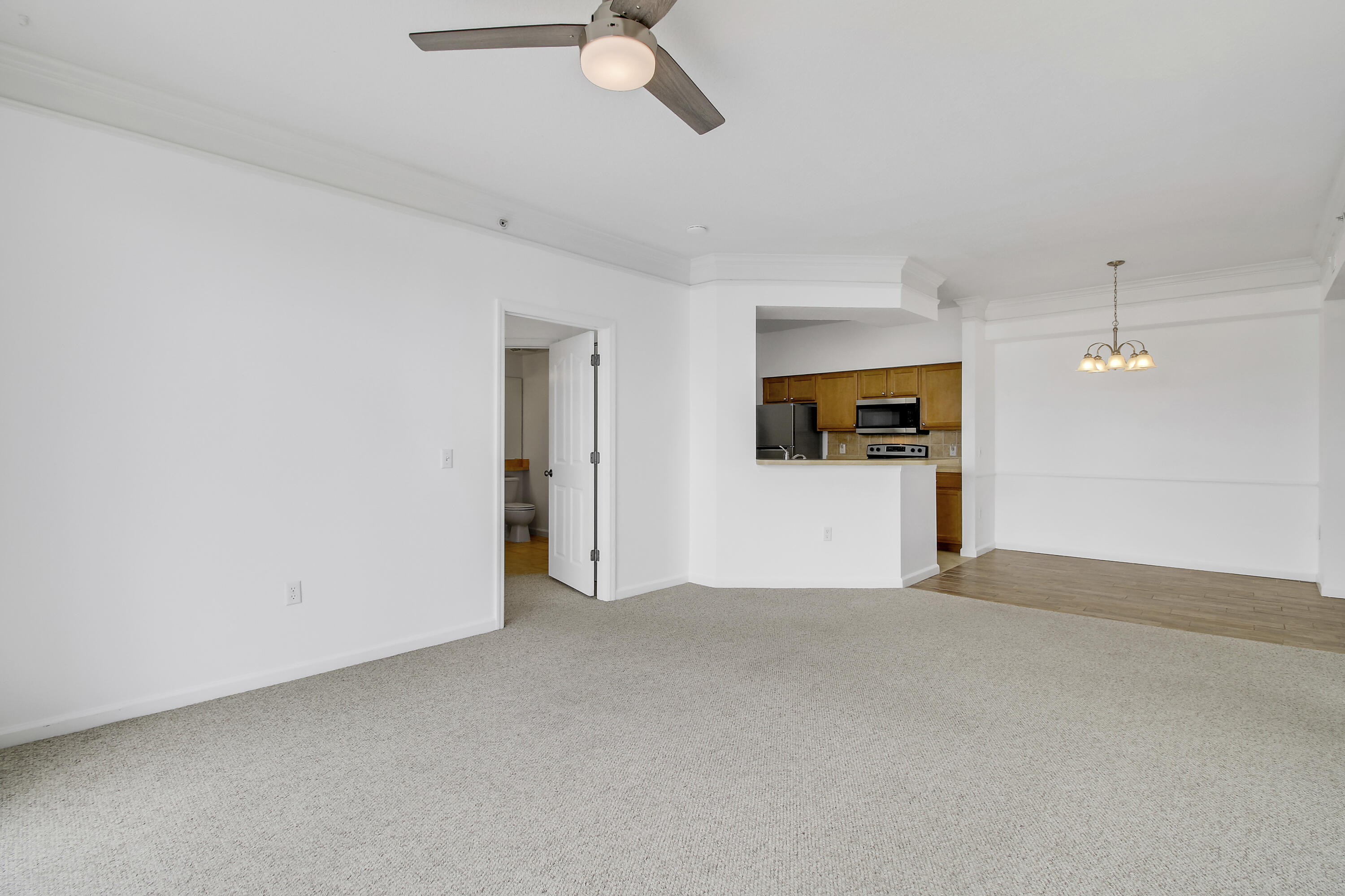 Vacant carpeted living area opening to a kitchen with wood cabinets and stainless steel appliances.