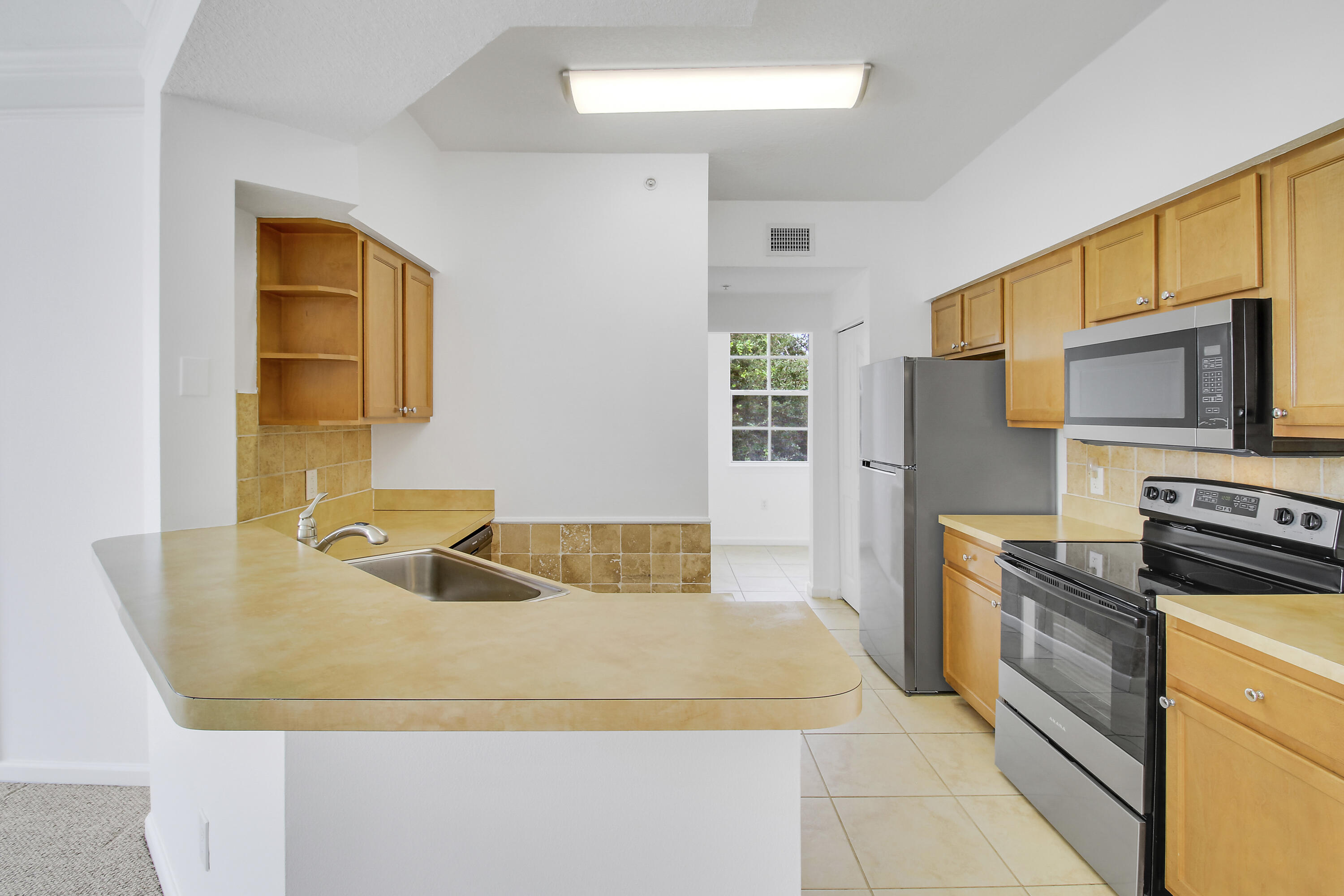 Kitchen with a broad tan peninsula, honey-colored cabinets, and stainless-steel appliances.