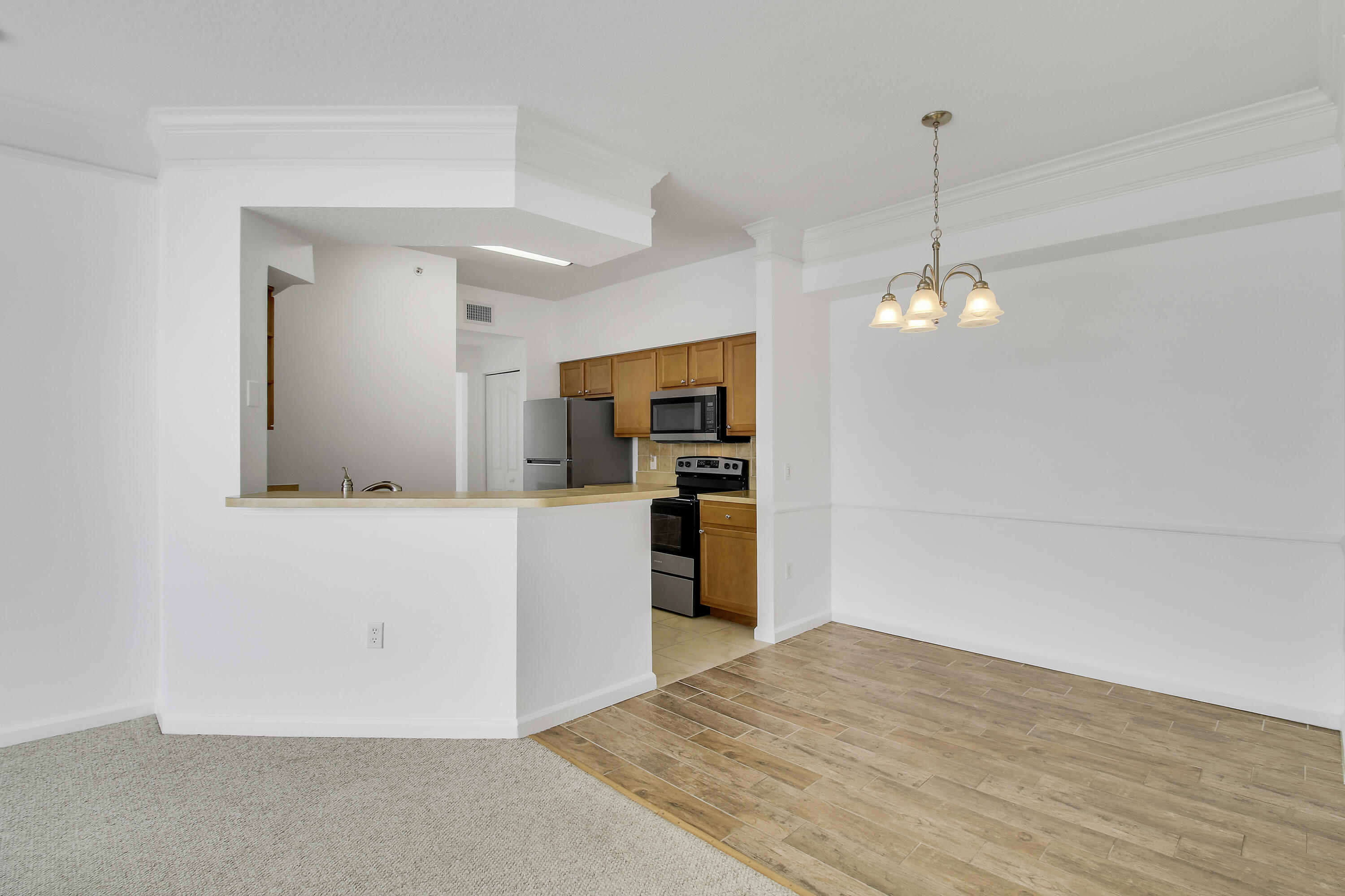 Open kitchen with a pass-through counter, wood cabinets, stainless steel appliances, and adjoining carpeted living space.