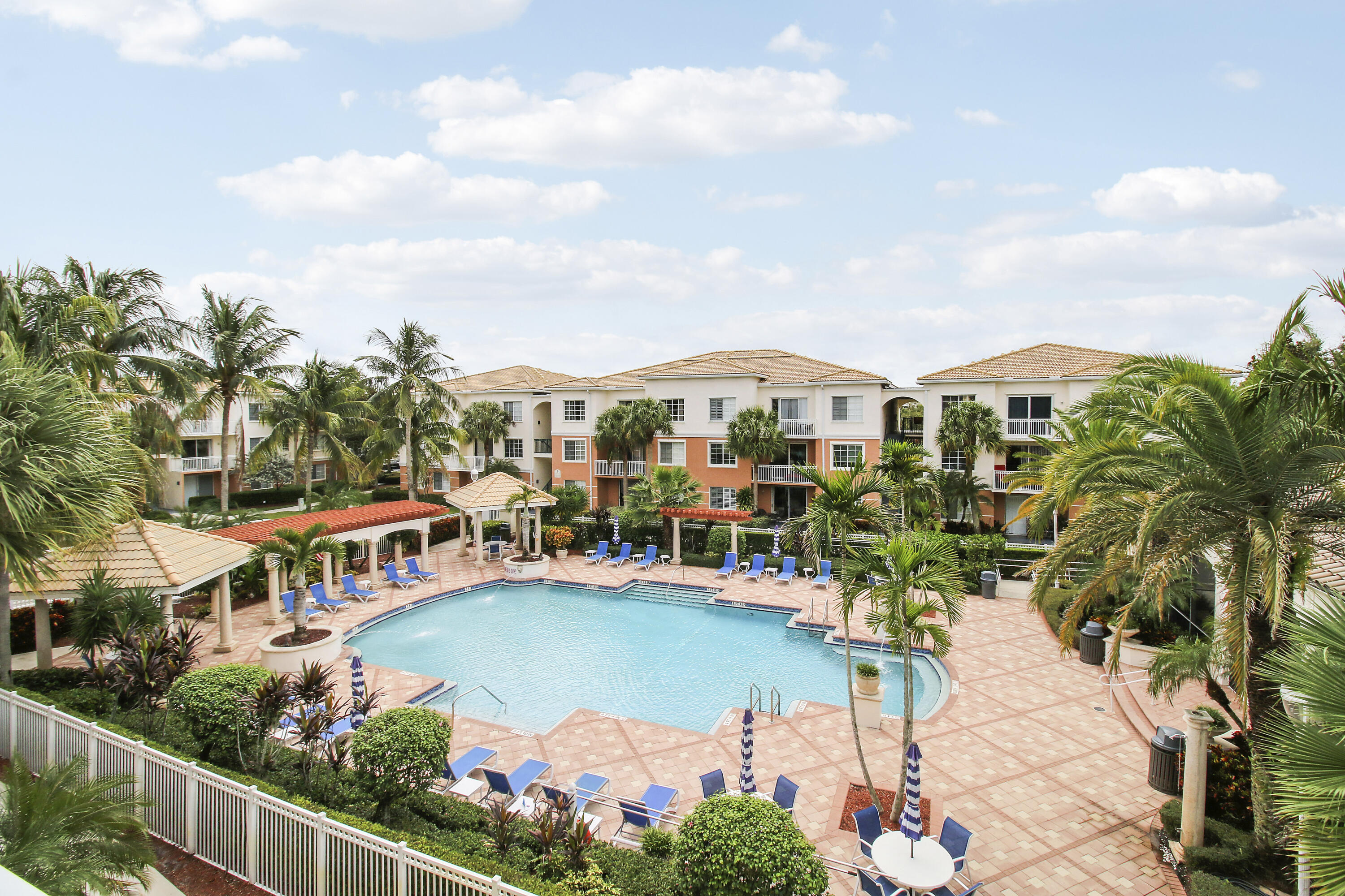 Condominium pool courtyard with palm trees, tiled deck, lounge chairs, and surrounding buildings.