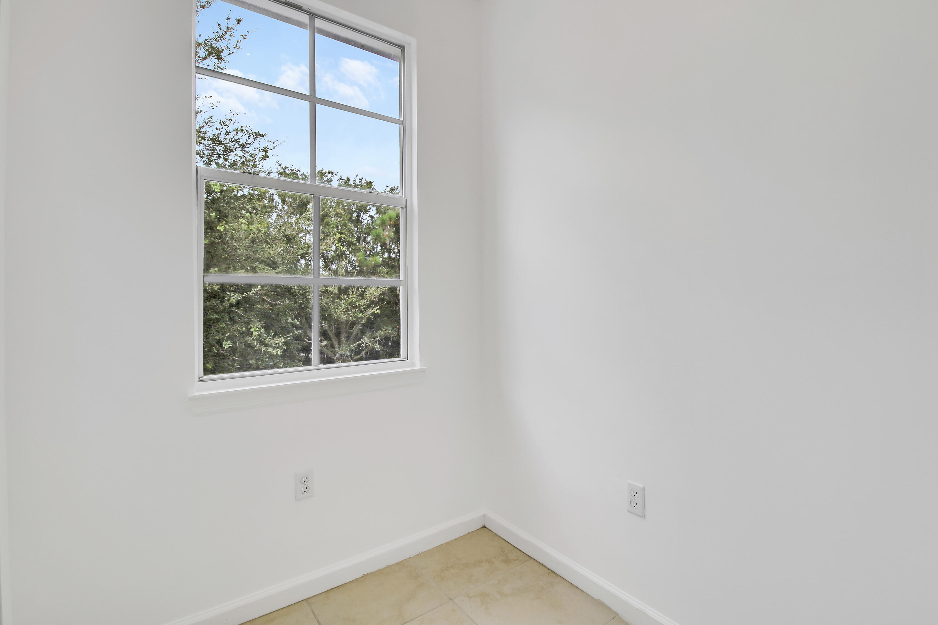 Empty room with beige tile flooring and a large window overlooking trees.