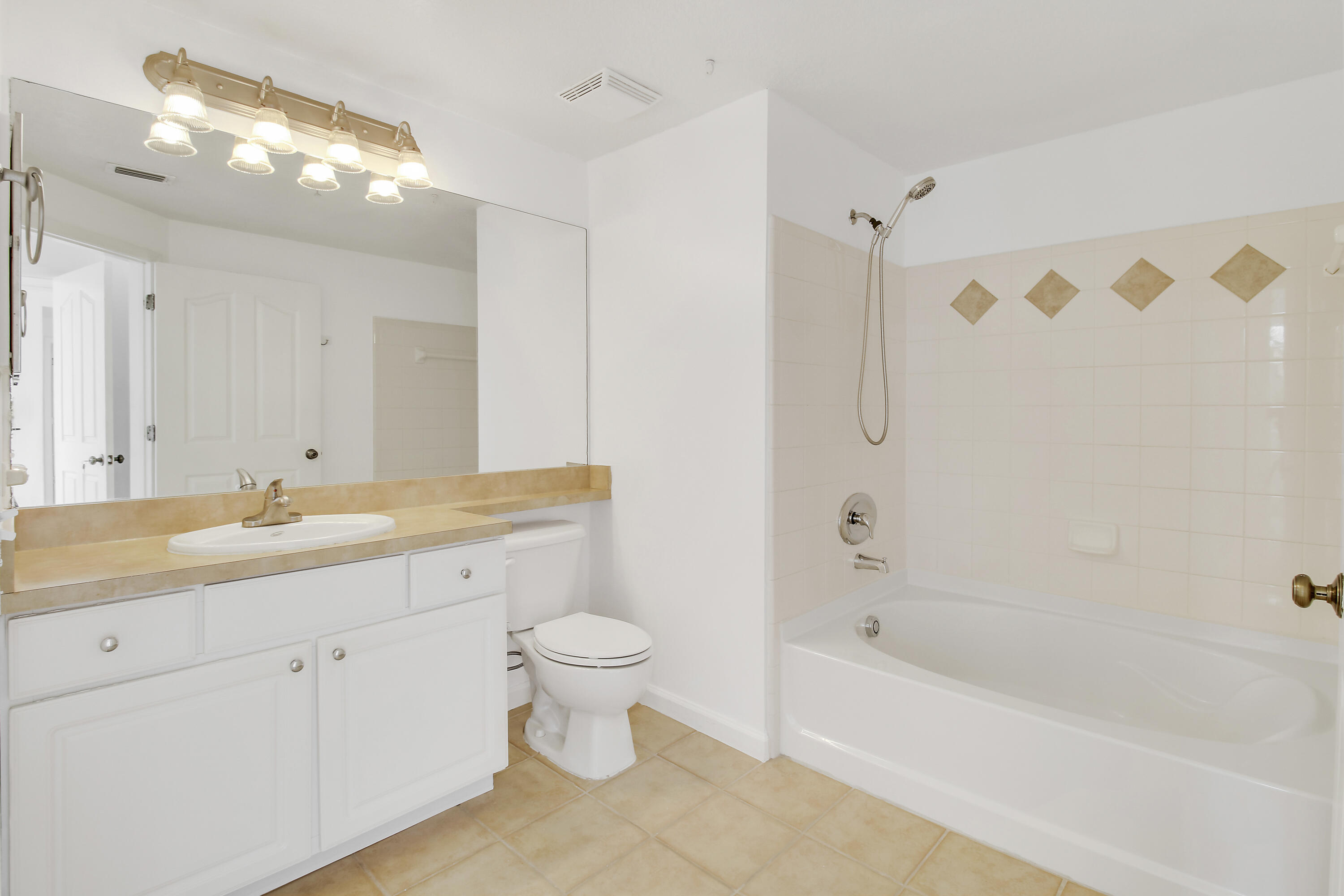 Bathroom with white vanity, toilet, and bathtub featuring beige diamond tile accents.