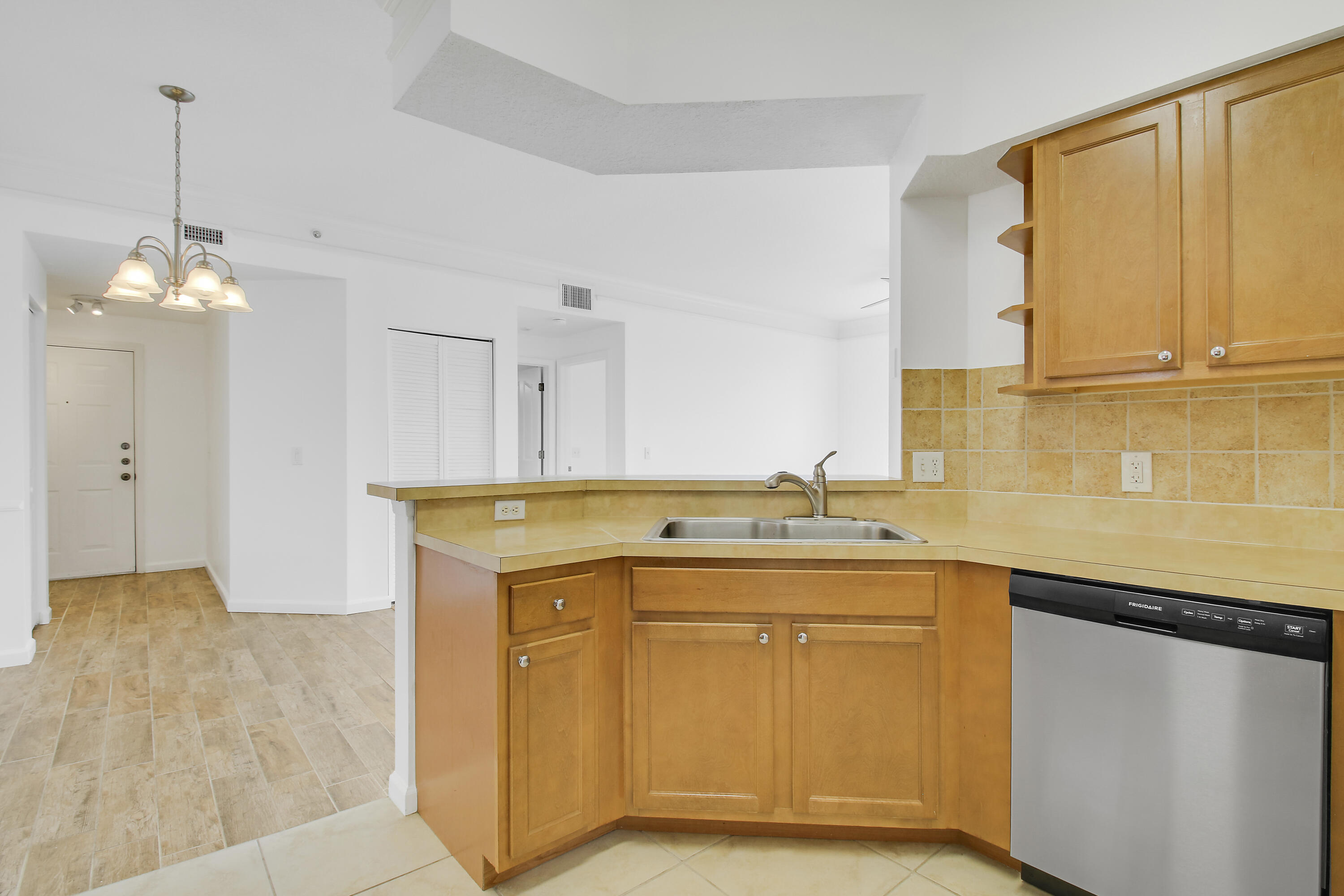 Kitchen with honey-colored cabinets, a corner sink, tan tile backsplash, and stainless steel dishwasher.
