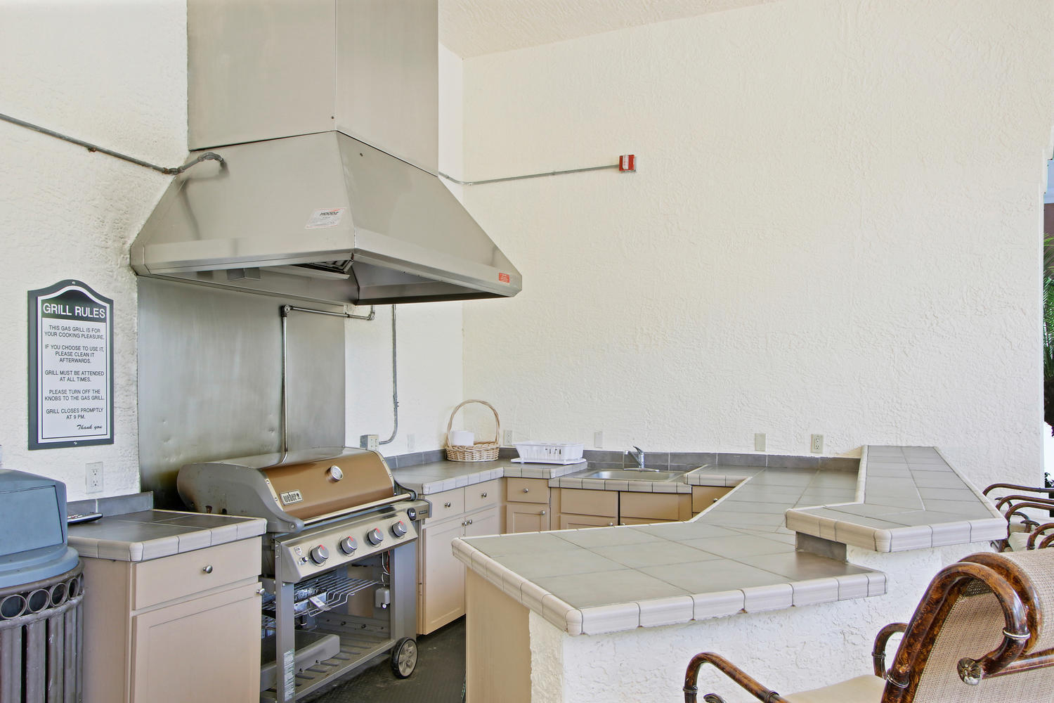 Outdoor kitchen with stainless-steel grill, large exhaust hood, tiled counters, and raised serving bar.