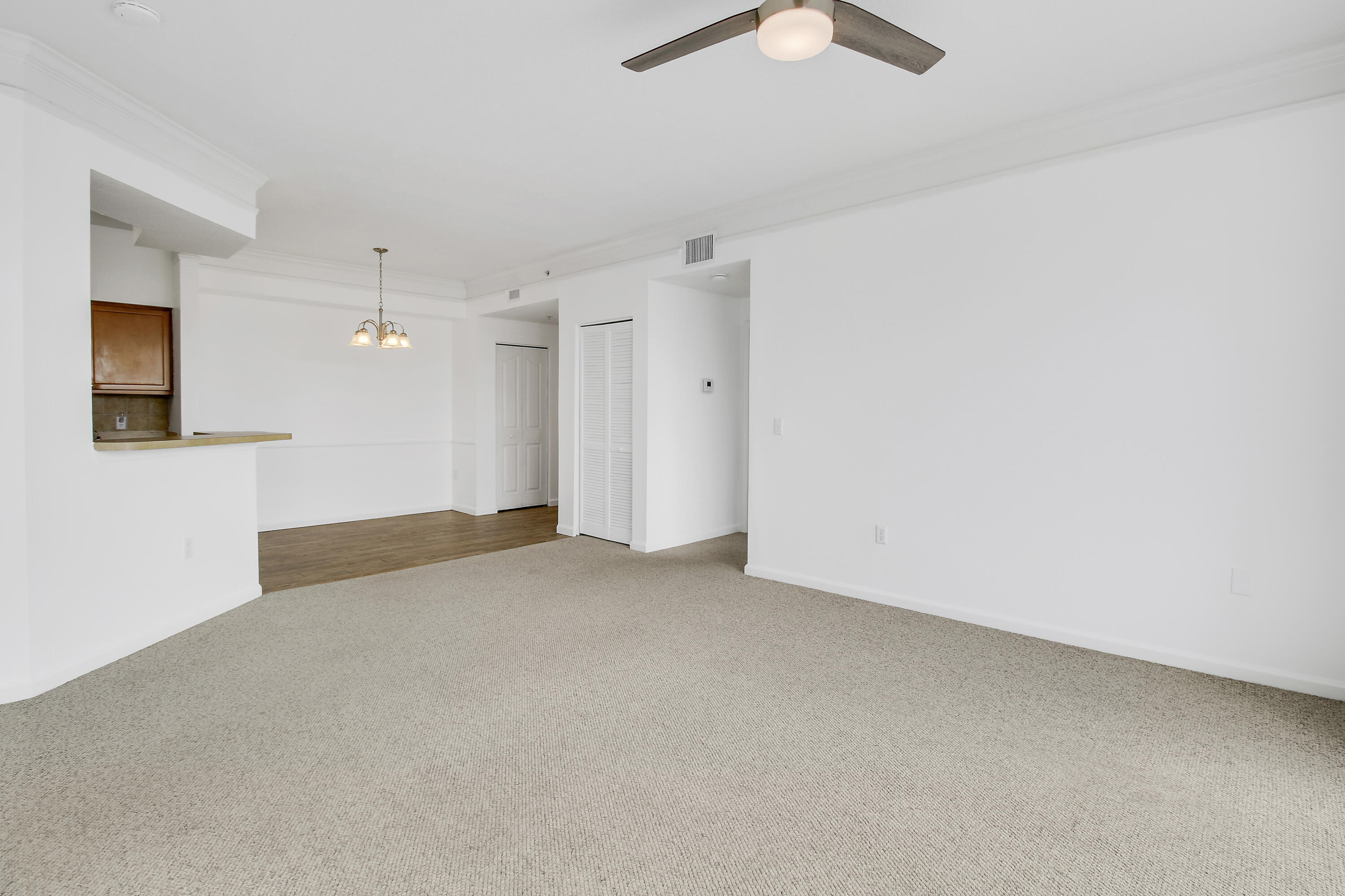 Vacant living and dining area with beige carpet, ceiling fan, and kitchen pass-through.