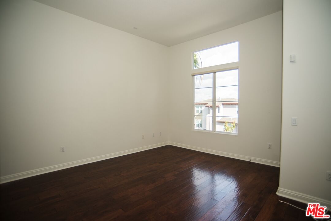 Vacant room with dark hardwood floors, a high ceiling, and a tall window.