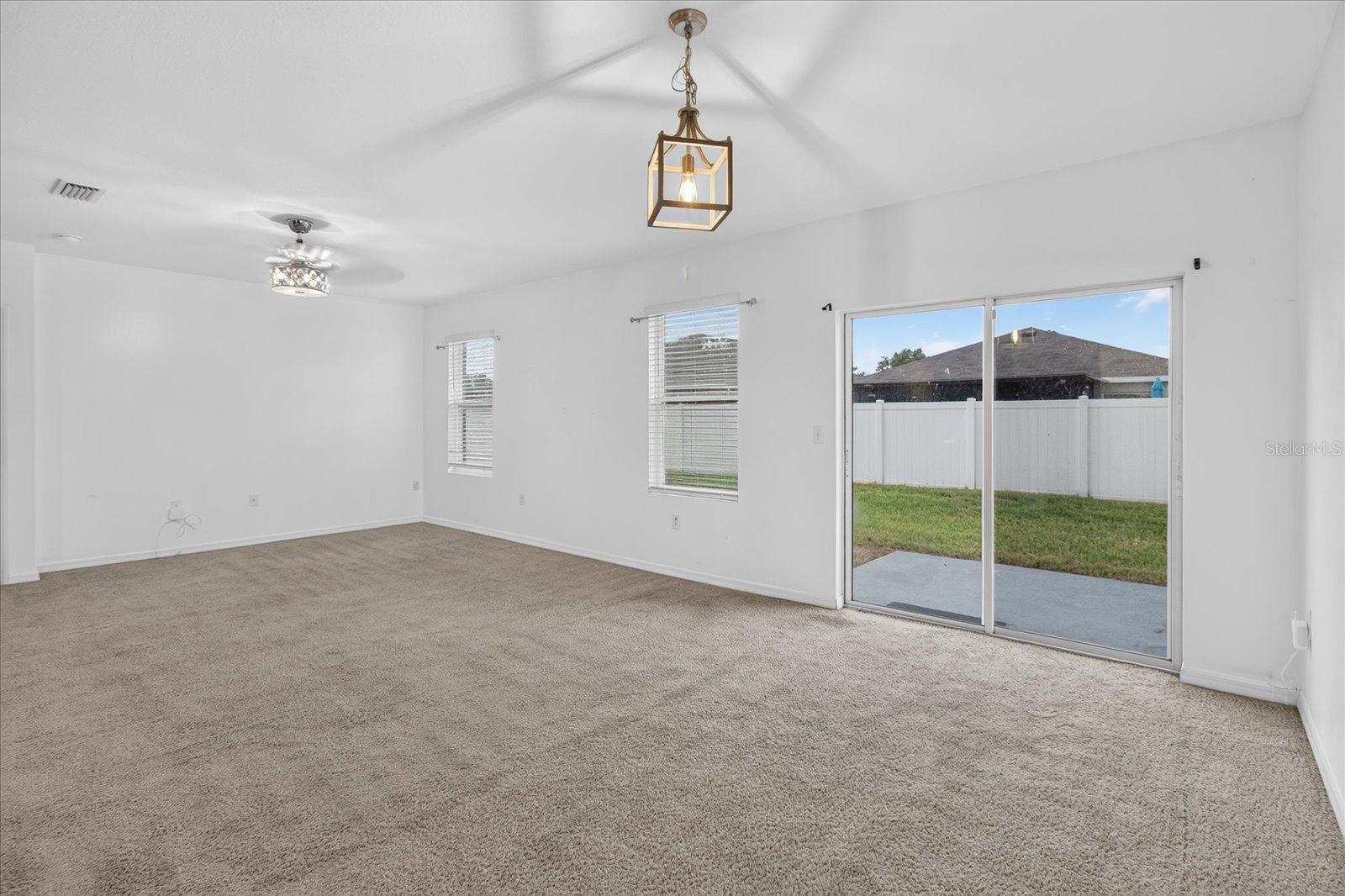 Empty carpeted living room with a ceiling fan and sliding glass doors to a fenced backyard.