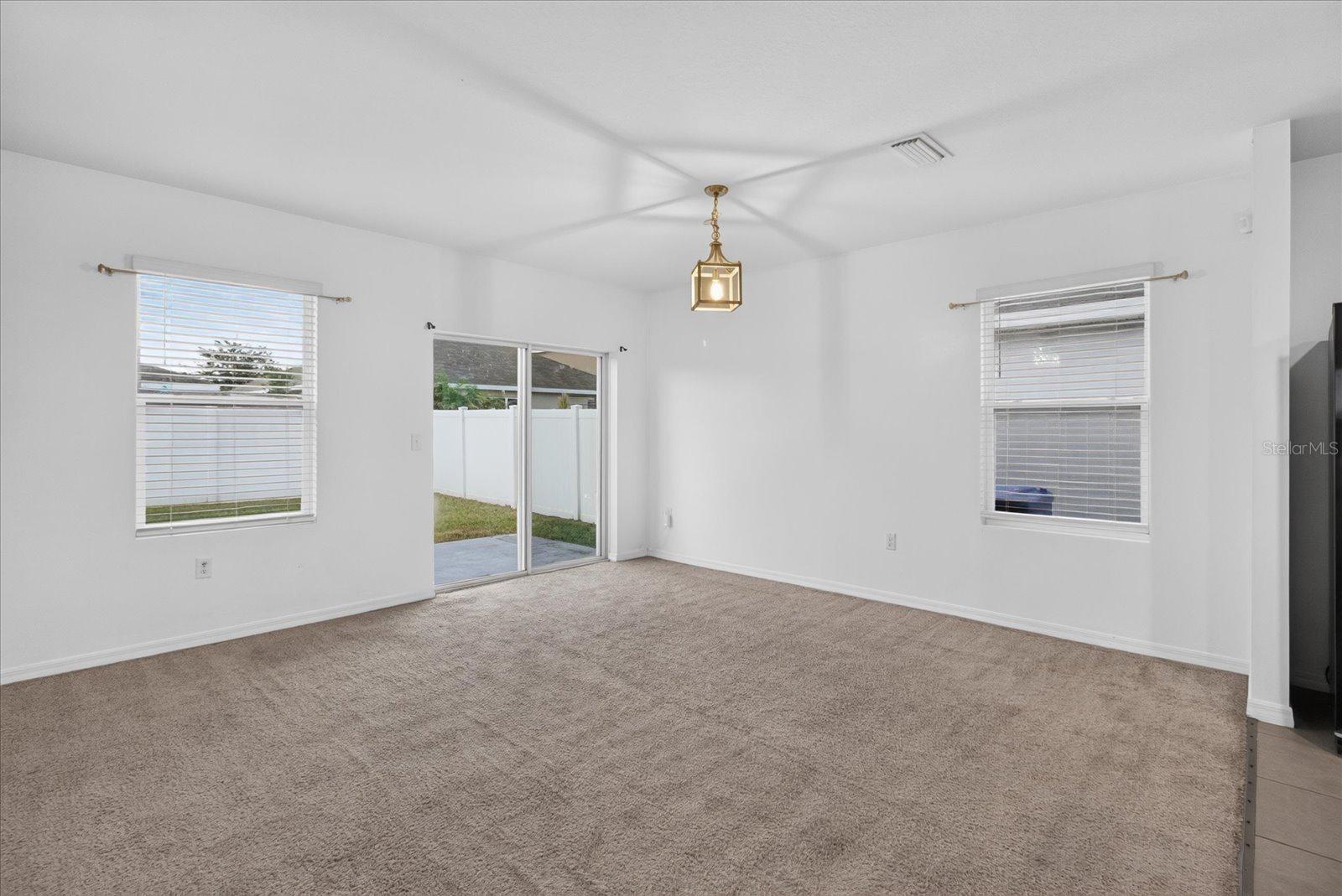 Unfurnished living room with beige carpet and sliding glass doors opening to a fenced yard.