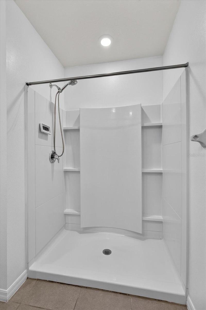 Walk-in shower with a chrome handheld showerhead and built-in shelves flanking a central panel.
