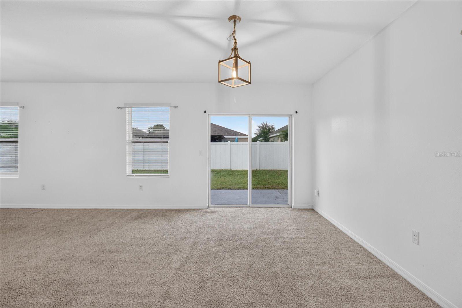 Empty carpeted living room with a high ceiling, lantern light, and sliding glass door to the backyard.