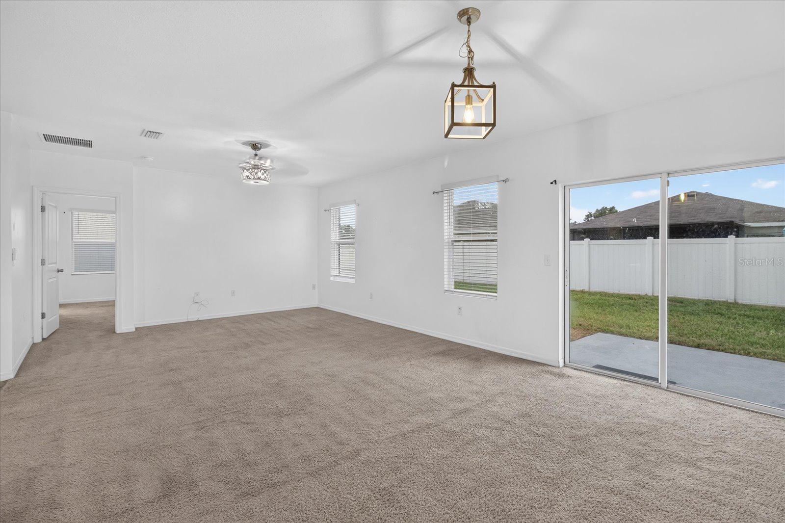 Empty carpeted living area with a ceiling fan and sliding glass doors to the fenced yard.