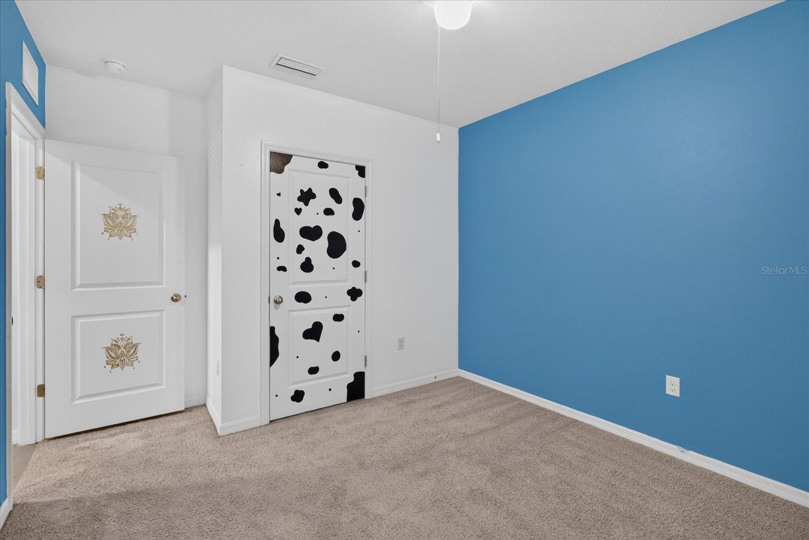 Empty carpeted room with a bright blue accent wall and a cow-print decorated door.