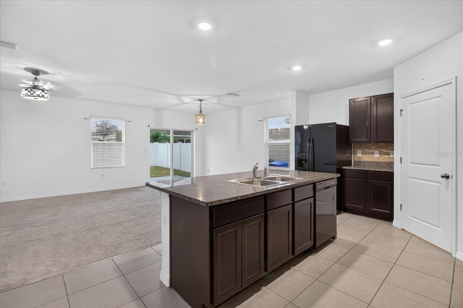 Open kitchen with a large dark-cabinet island adjoining a carpeted living area and sliding glass doors.