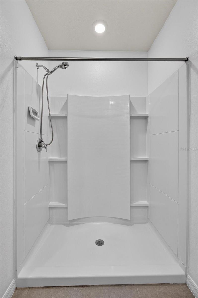 White walk-in shower with chrome fixtures, built-in shelves, and a tall curved center panel.