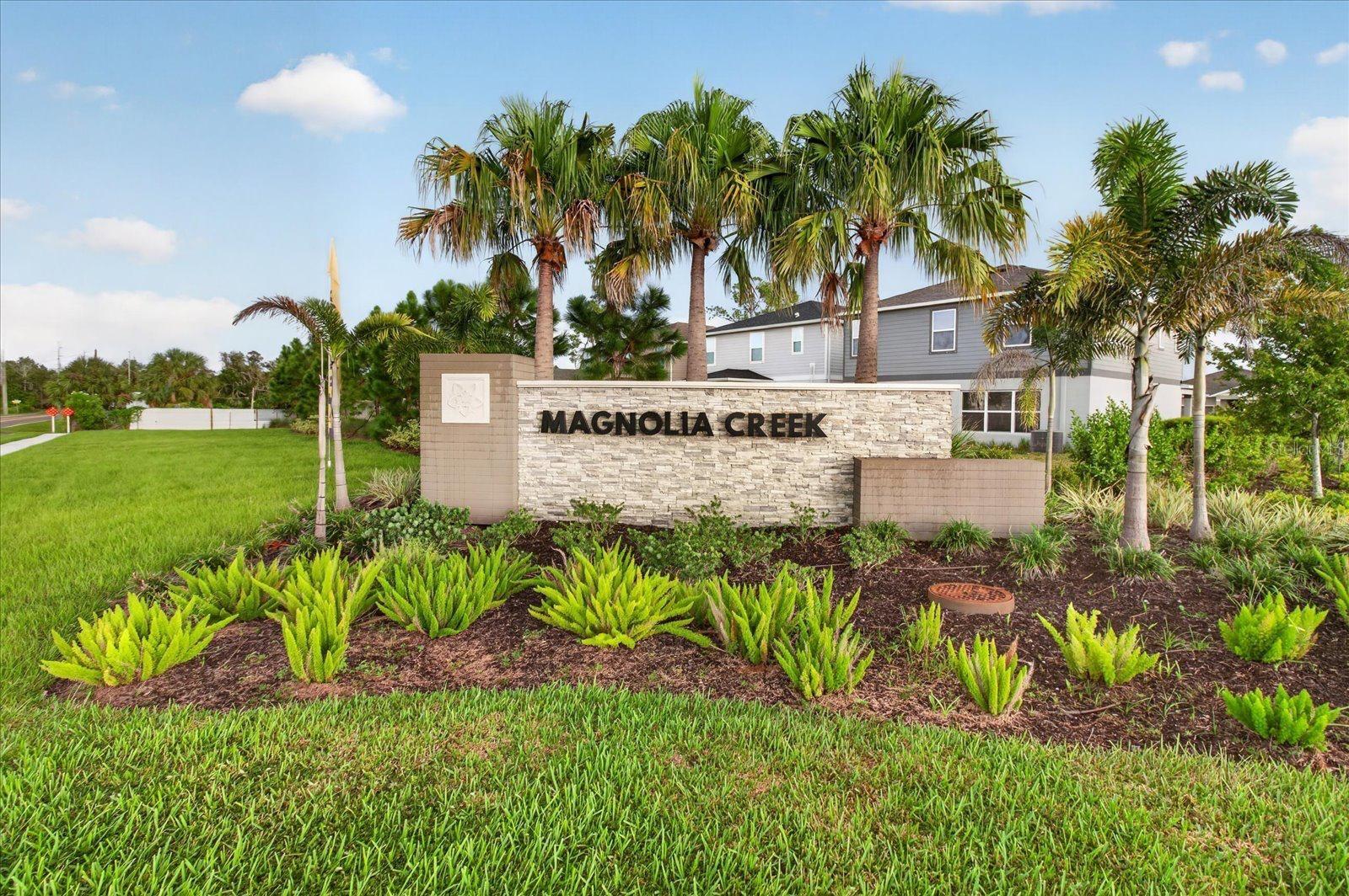 Magnolia Creek community entrance sign surrounded by palm trees and landscaped greenery.