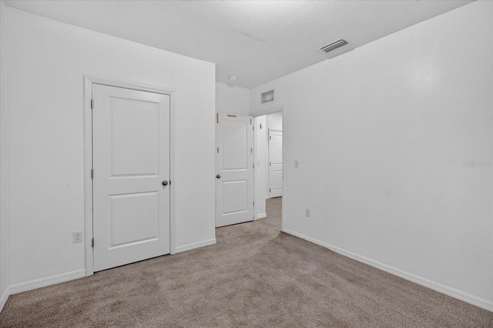 Empty bedroom with beige carpeting, white walls, and multiple paneled doors.
