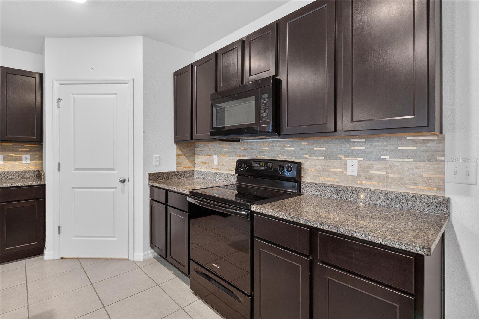 Kitchen with dark wood cabinets, granite counters, mosaic backsplash, and black appliances.