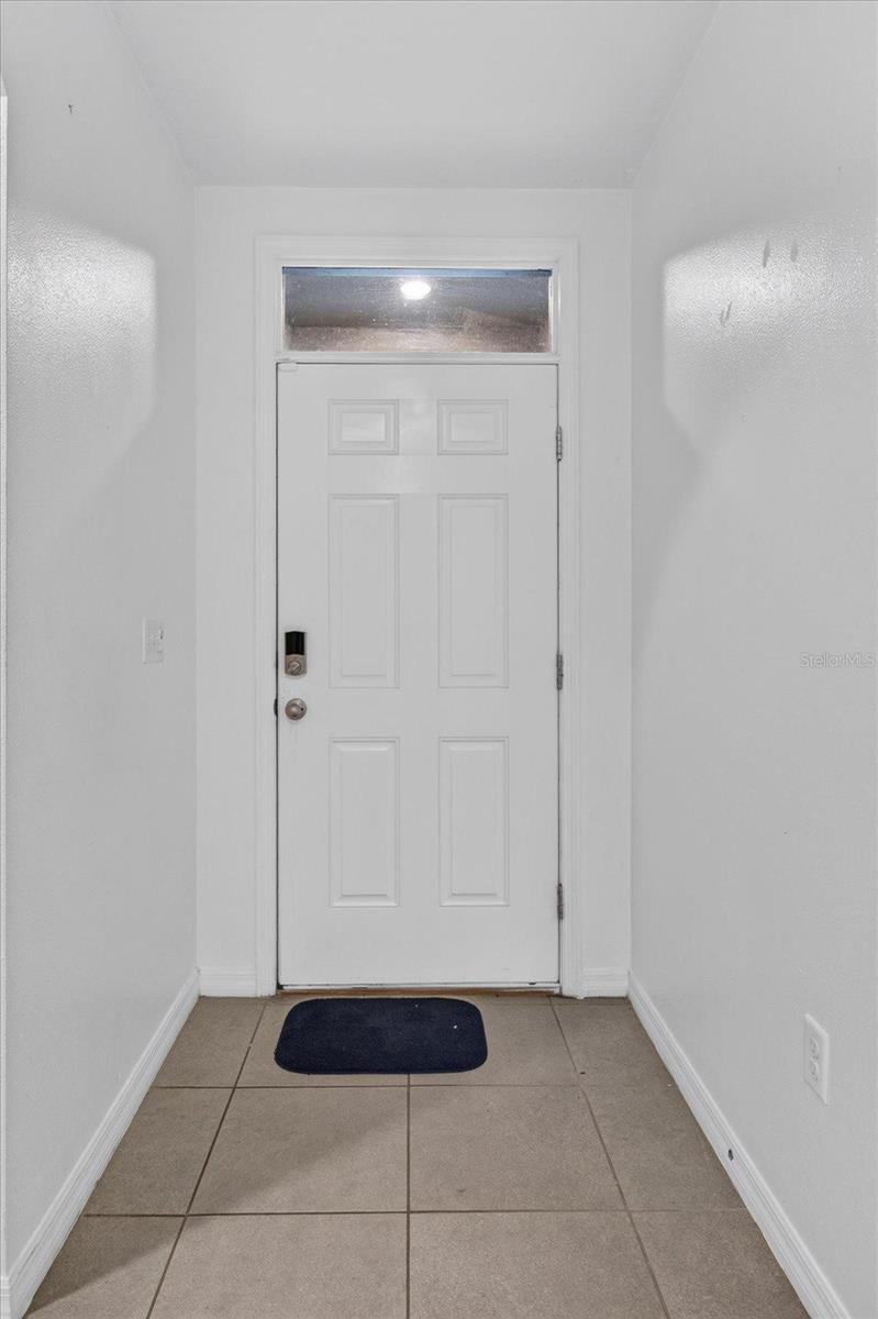 Entryway with a white front door, transom window, electronic lock, and tiled floor.