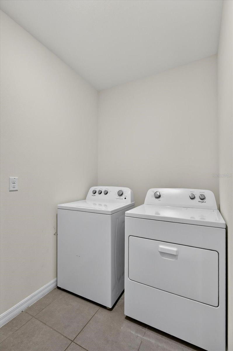 Laundry room with a white washer and front-loading dryer on a gray tile floor.