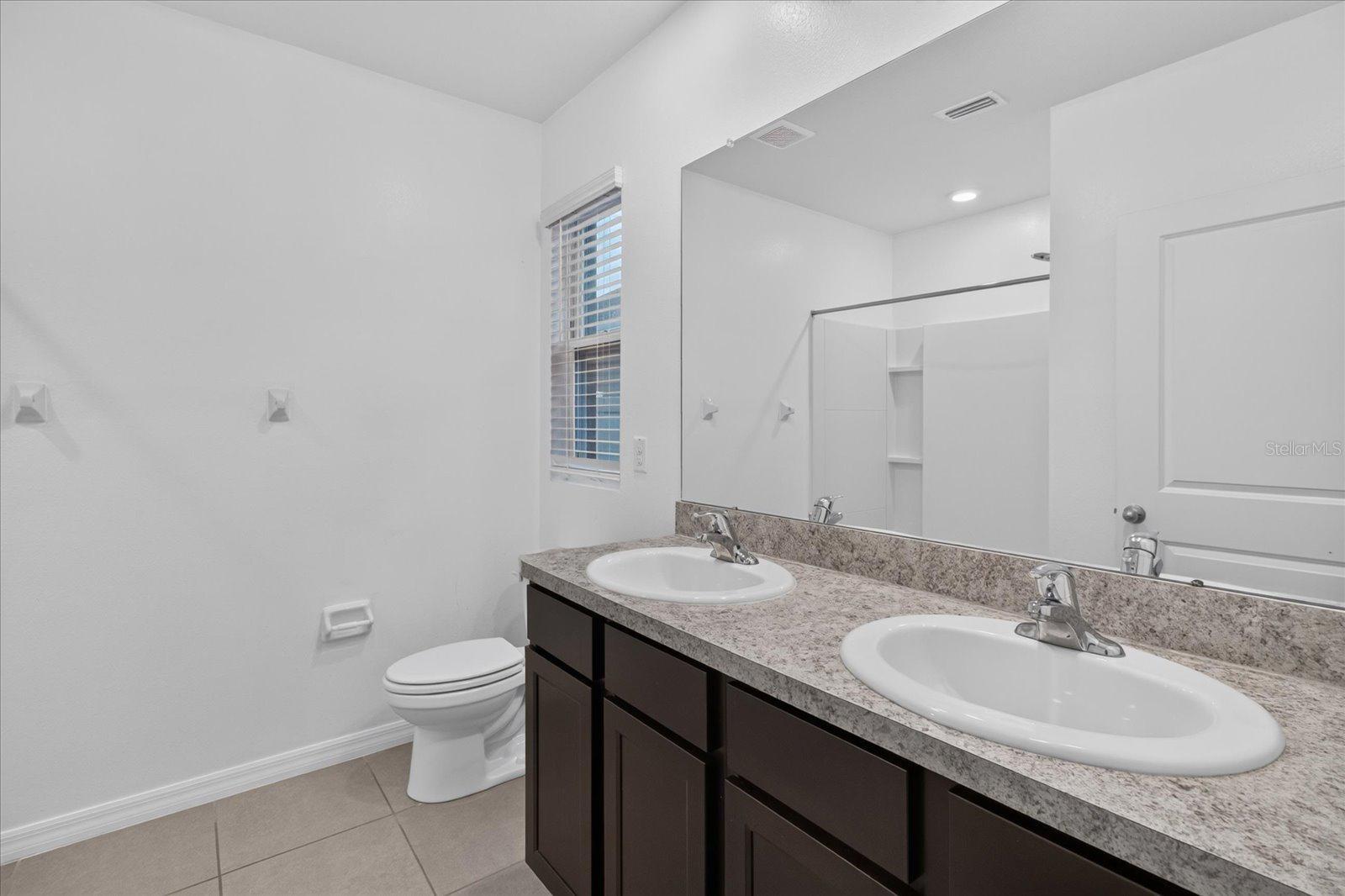 Bathroom with double-sink vanity, dark cabinets, large mirror, and tiled floor.