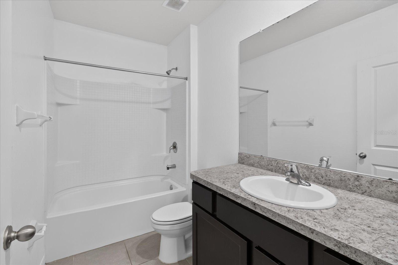 Bathroom with tub and shower, toilet, and dark vanity with granite countertop.