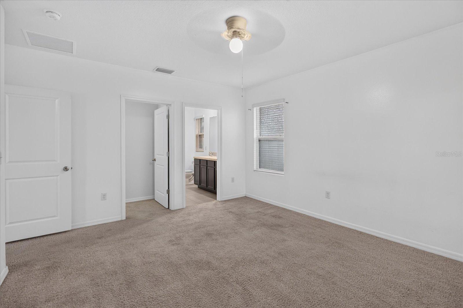 Empty carpeted bedroom with a window and an open doorway to a bathroom.