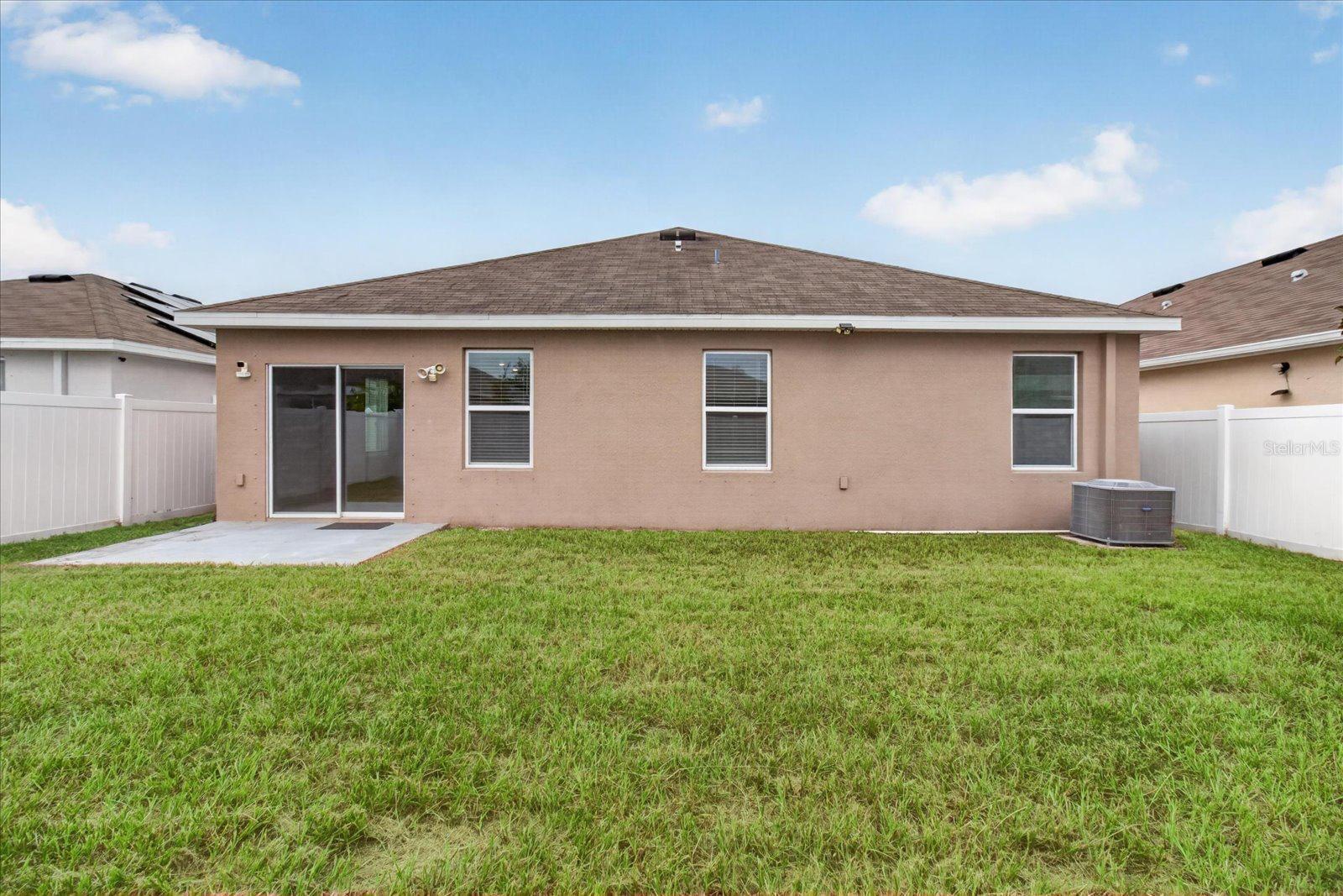 Rear of a tan single-story home with a fenced grassy yard and small concrete patio.