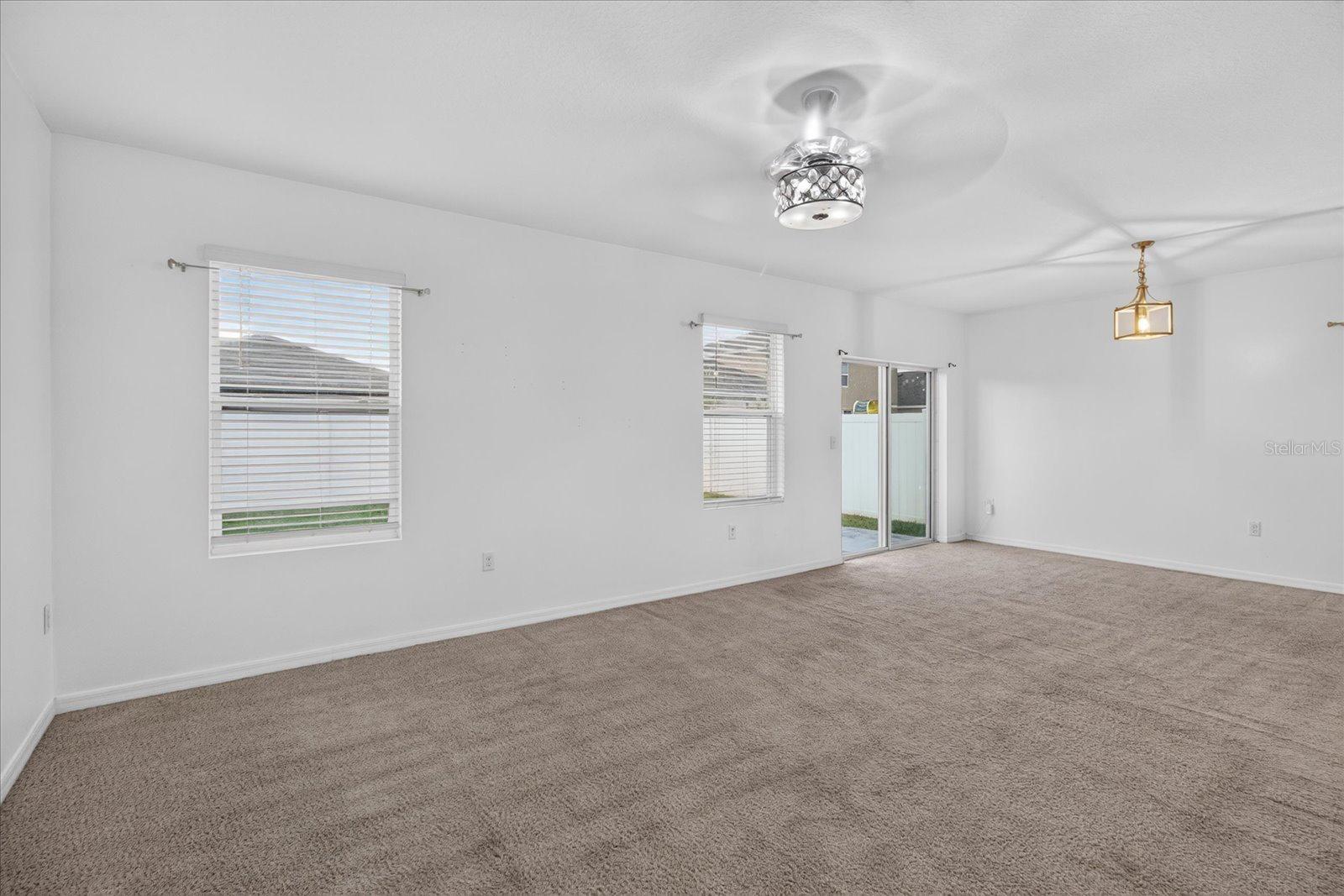Vacant carpeted living room with two windows, a sliding glass door, and a ceiling fan.