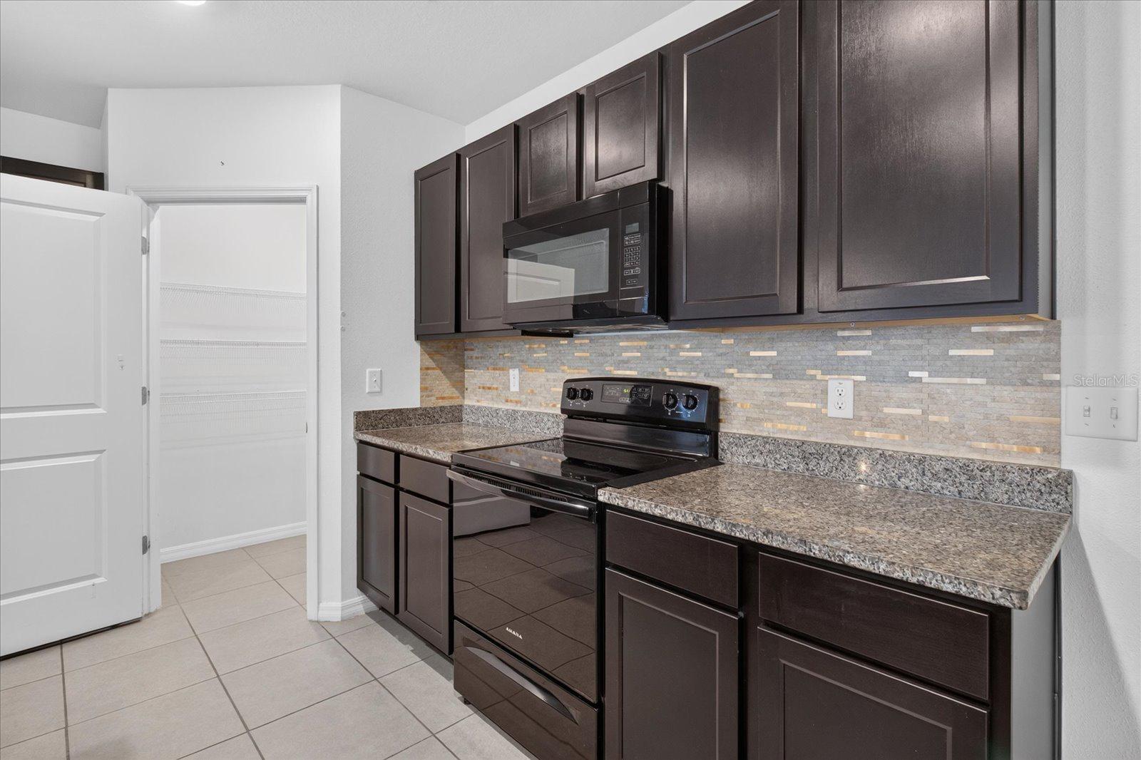 Kitchen with dark cabinets, granite counters, a mosaic backsplash, and black appliances.