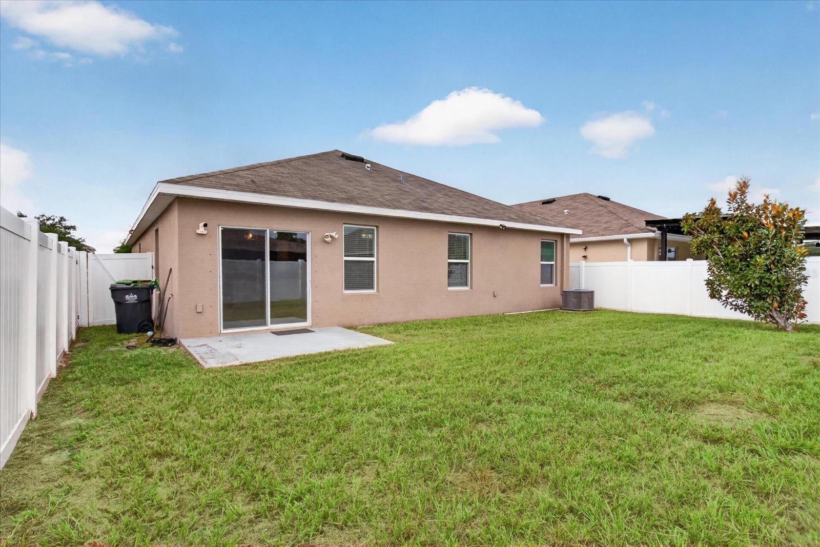 Tan single-story home with sliding glass doors and a fenced grassy backyard.