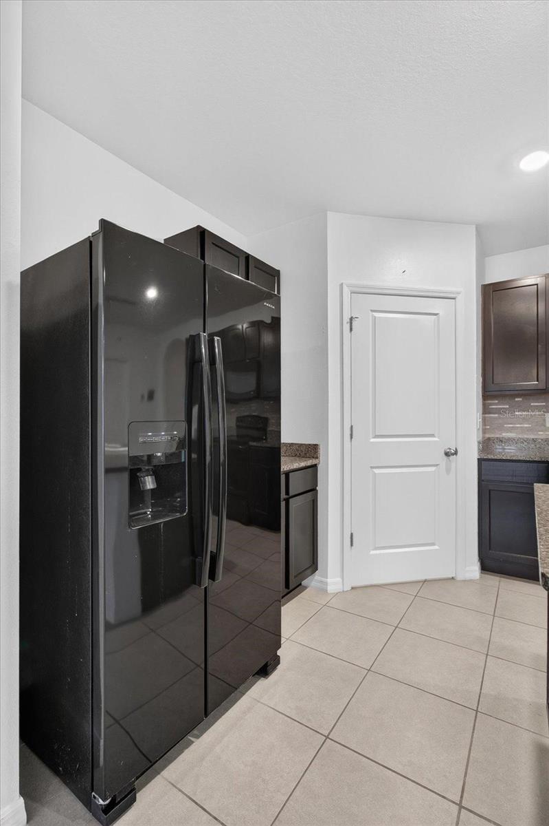 Kitchen with a black side-by-side refrigerator, dark cabinets, granite countertops, and beige tile flooring.