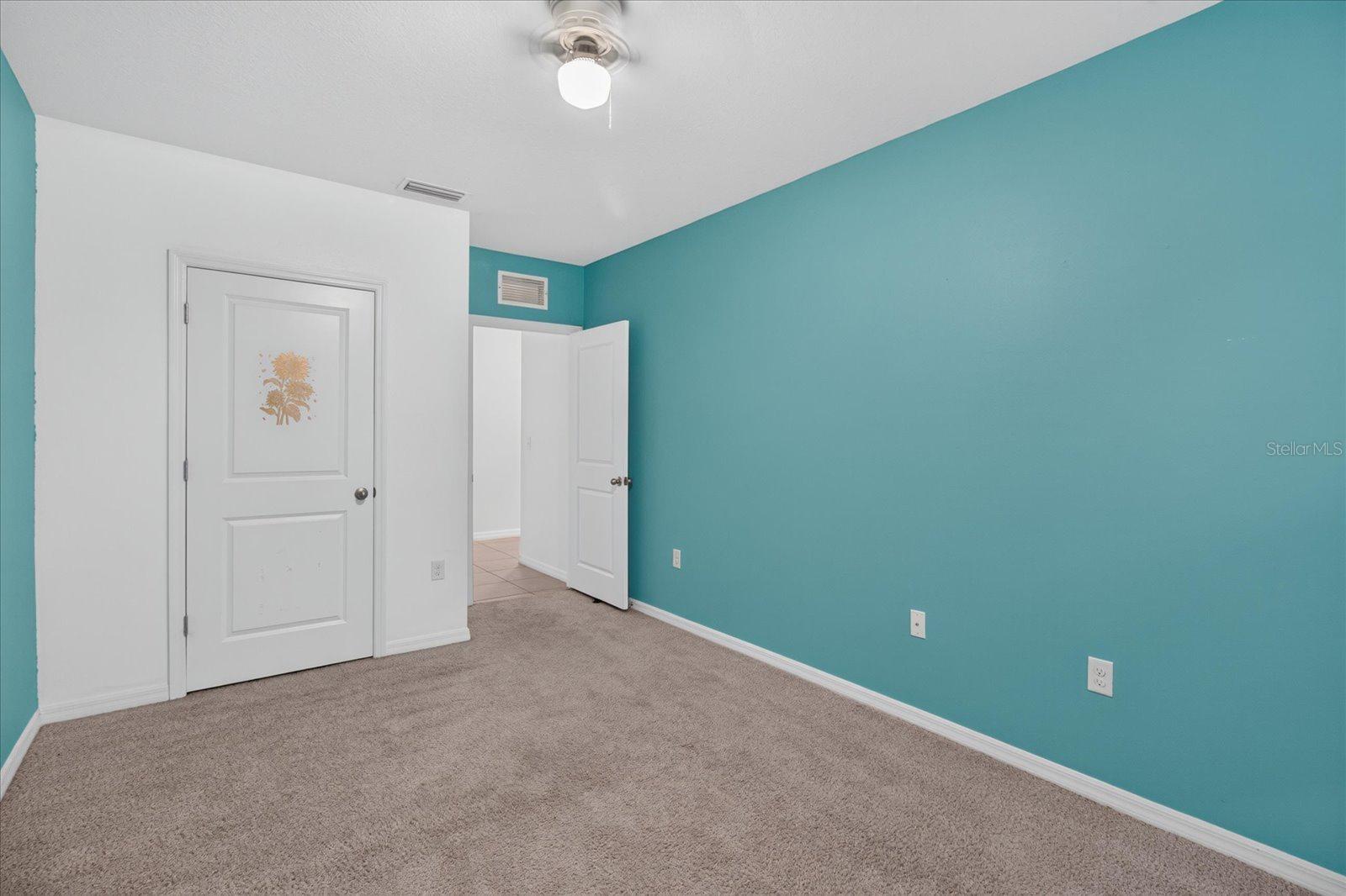 Empty bedroom with a teal wall, beige carpet, white doors, and a ceiling fan.