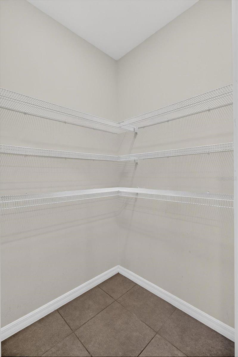 Empty walk-in closet with white wire shelving and brown tile flooring.