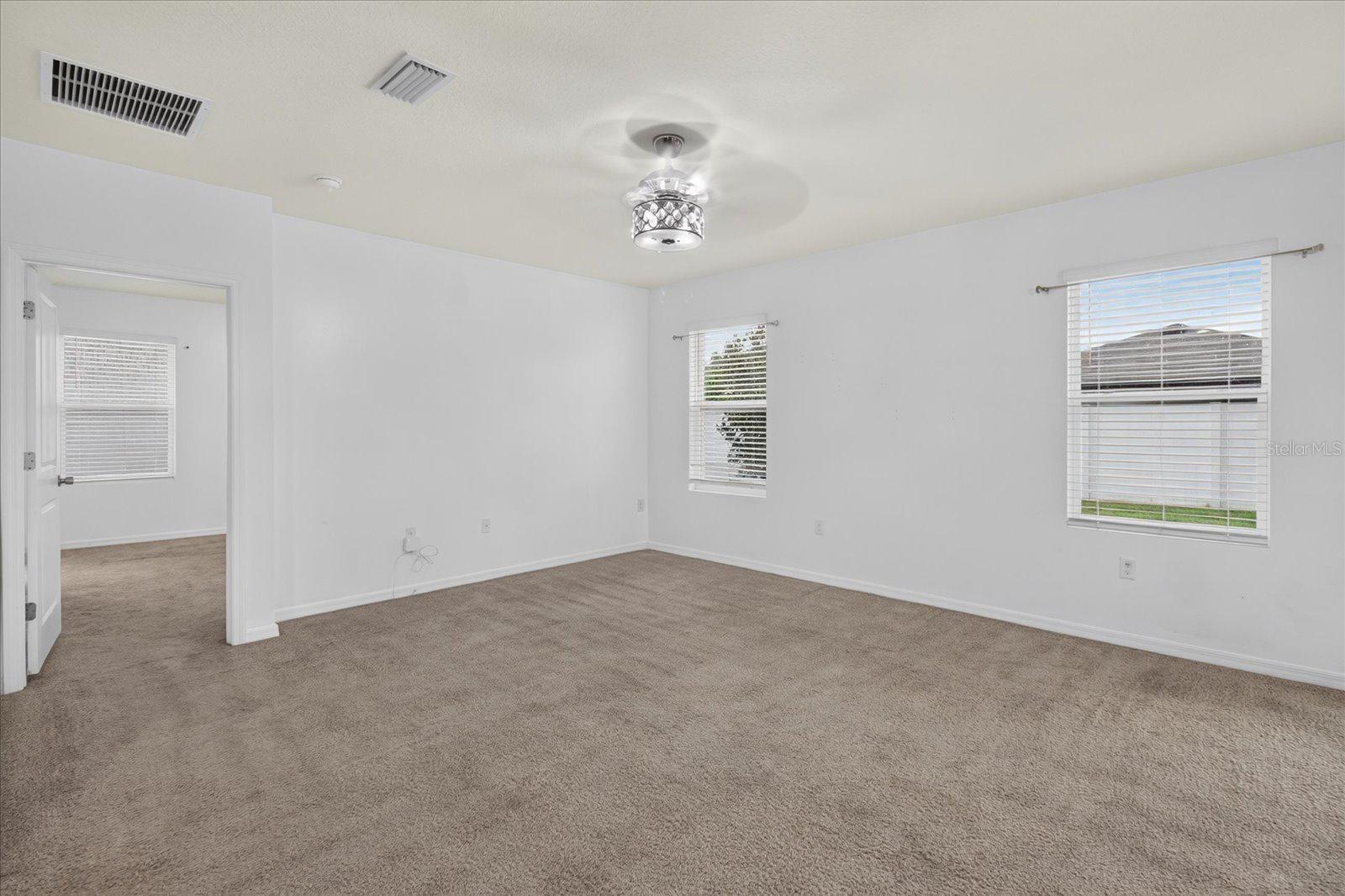 Empty carpeted bedroom with white walls, two windows, and a ceiling fan with light.
