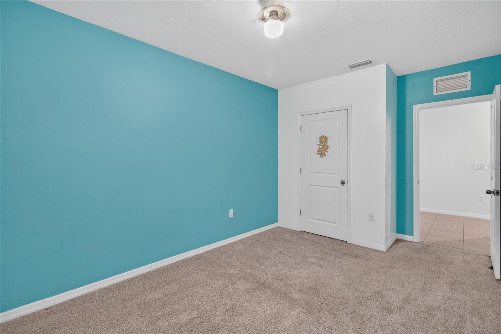 Empty carpeted bedroom with a turquoise accent wall and open doorway to a tiled area.