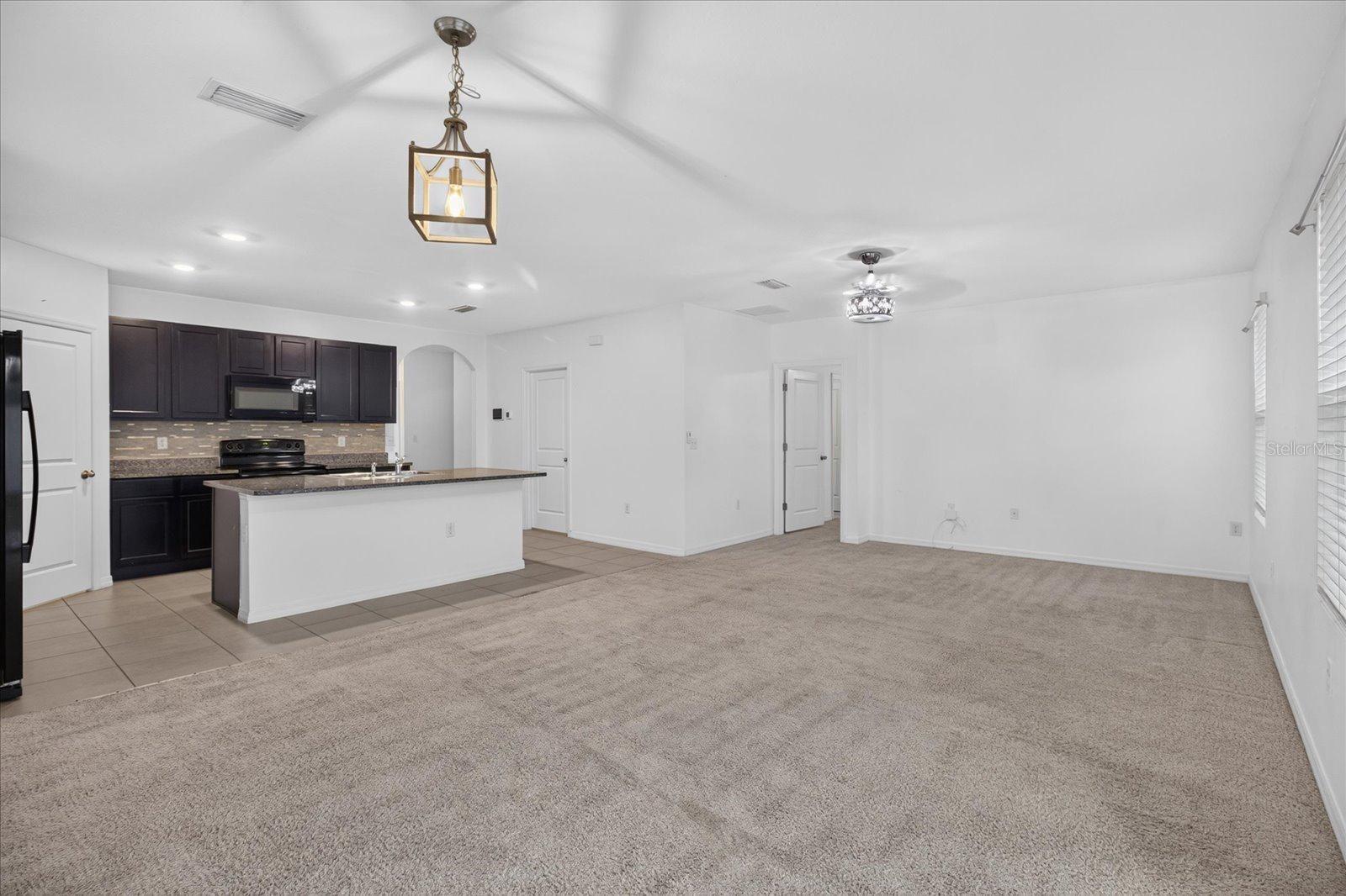 Open living room and kitchen with dark cabinets, a white island, and beige carpet.