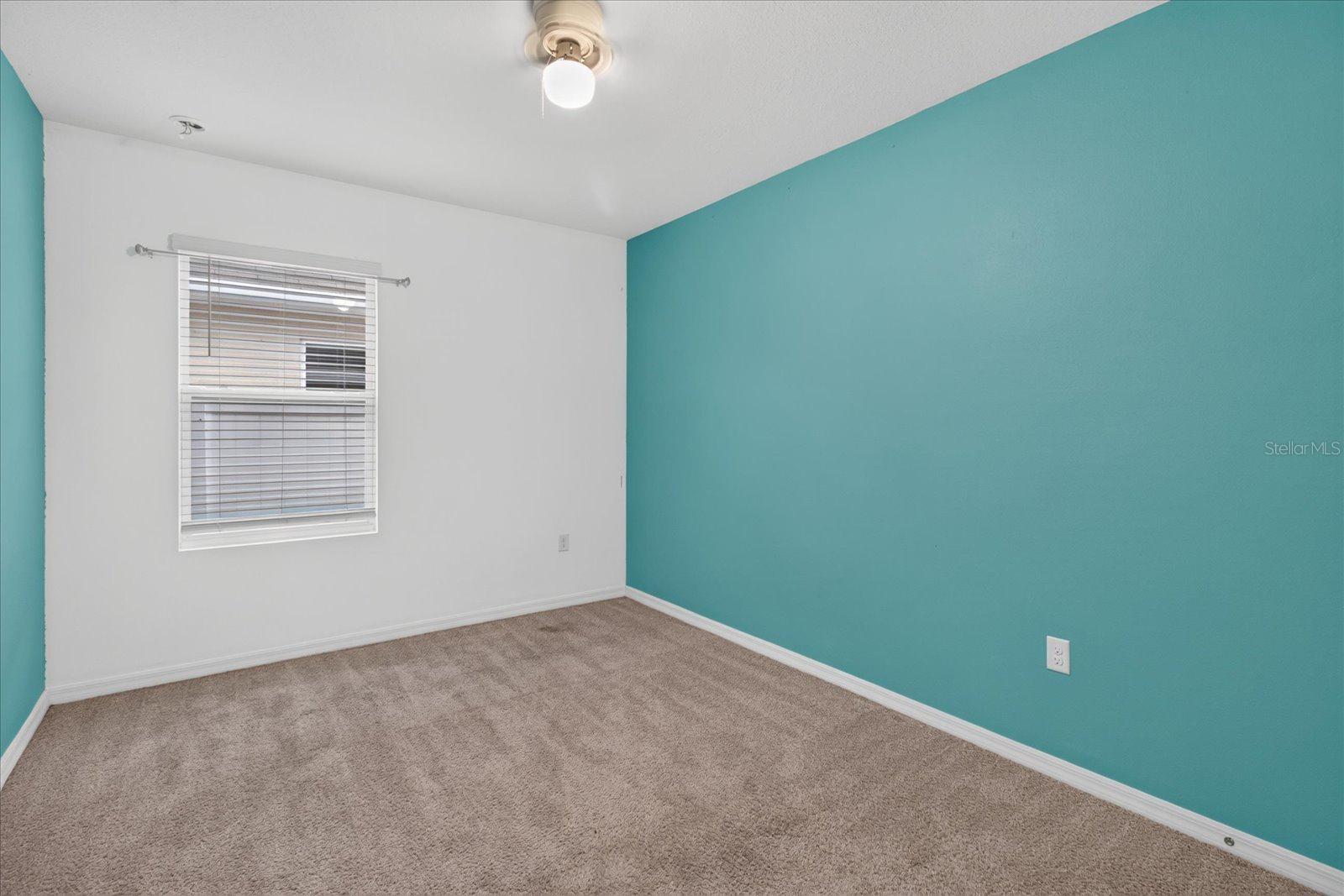 Unfurnished bedroom with beige carpet, a teal accent wall, and a window with blinds.