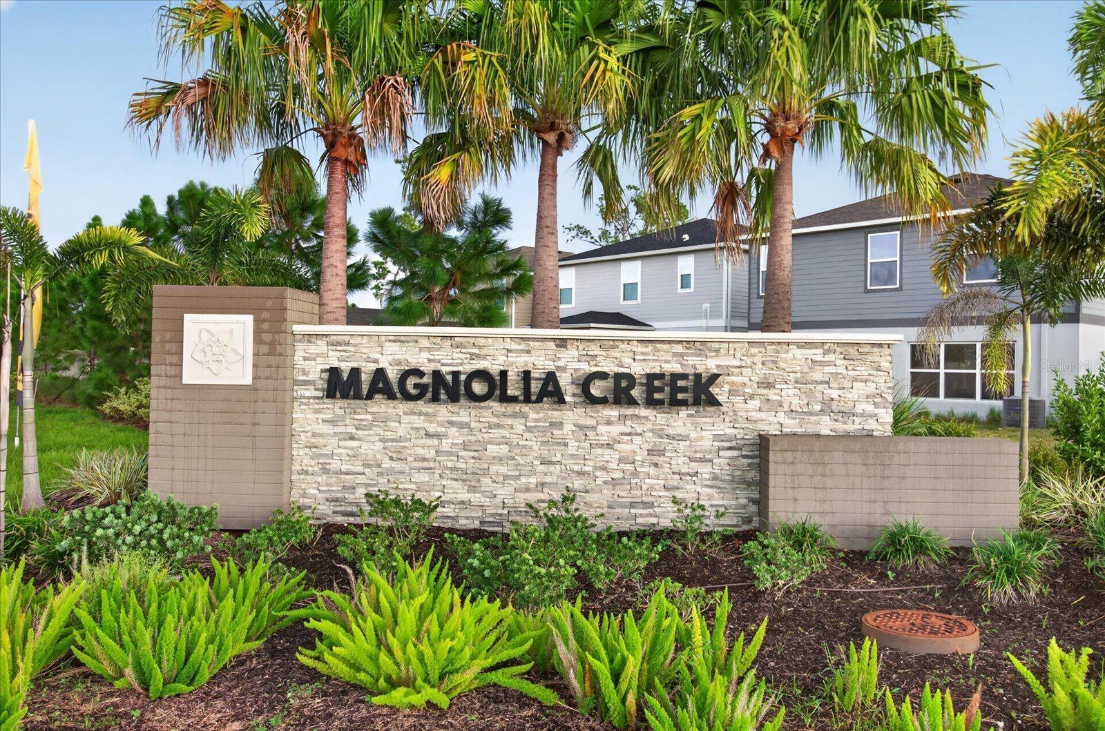 Magnolia Creek community entrance sign amid palm trees and landscaped greenery.