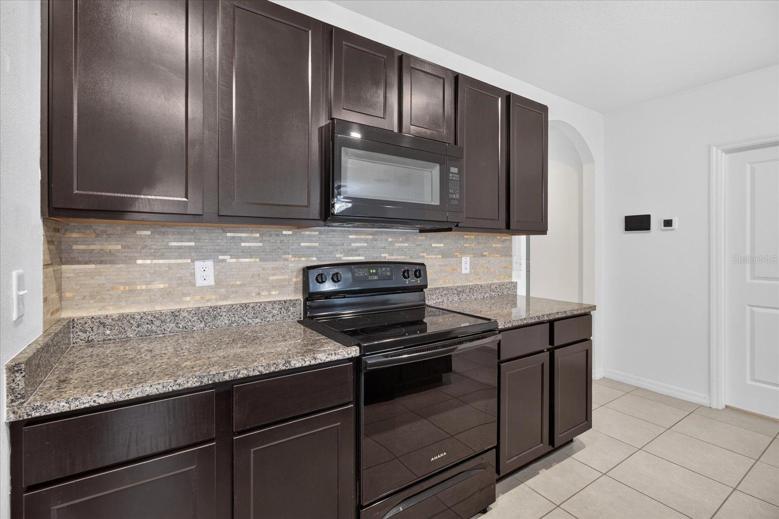 Kitchen with dark cabinets, granite counters, mosaic backsplash, and black appliances.