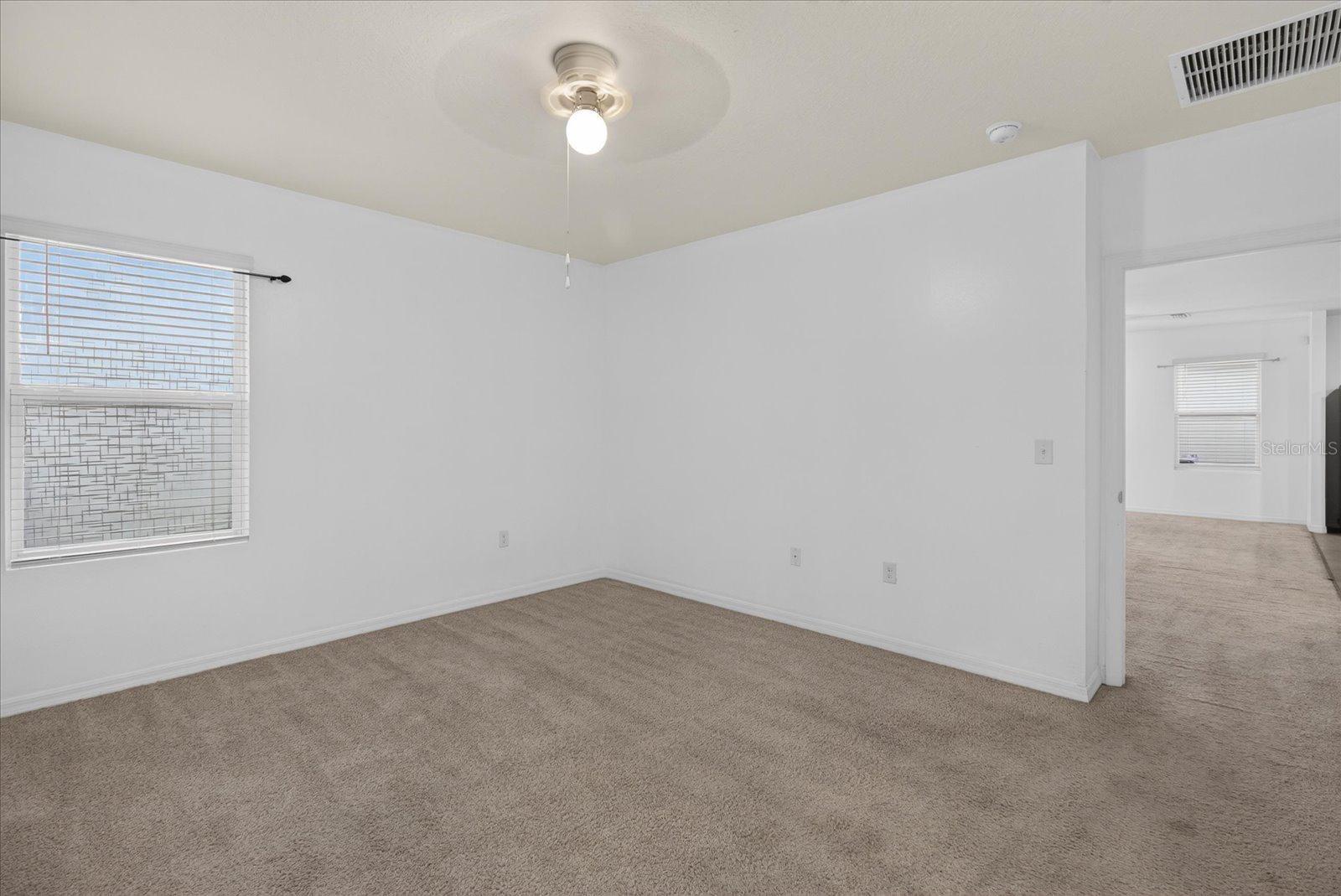 Empty carpeted bedroom with window blinds and a ceiling fan with light.