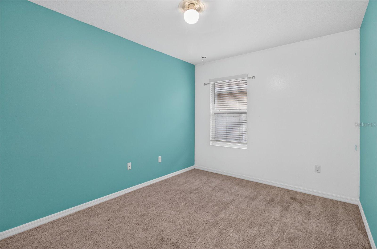 Empty carpeted room with a teal accent wall and a window with blinds.