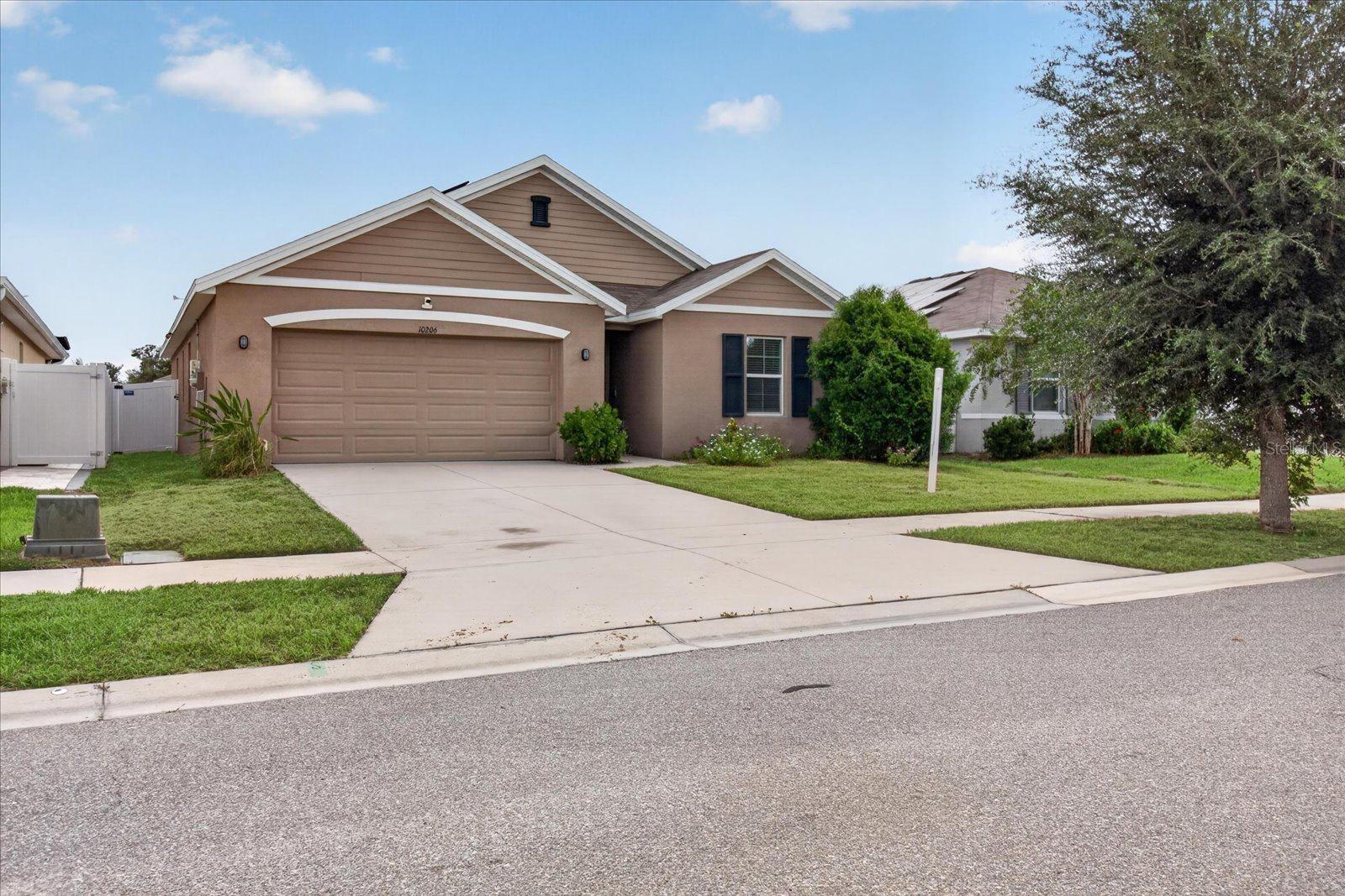 Tan single-story home with a two-car garage, wide driveway, and landscaped front lawn.