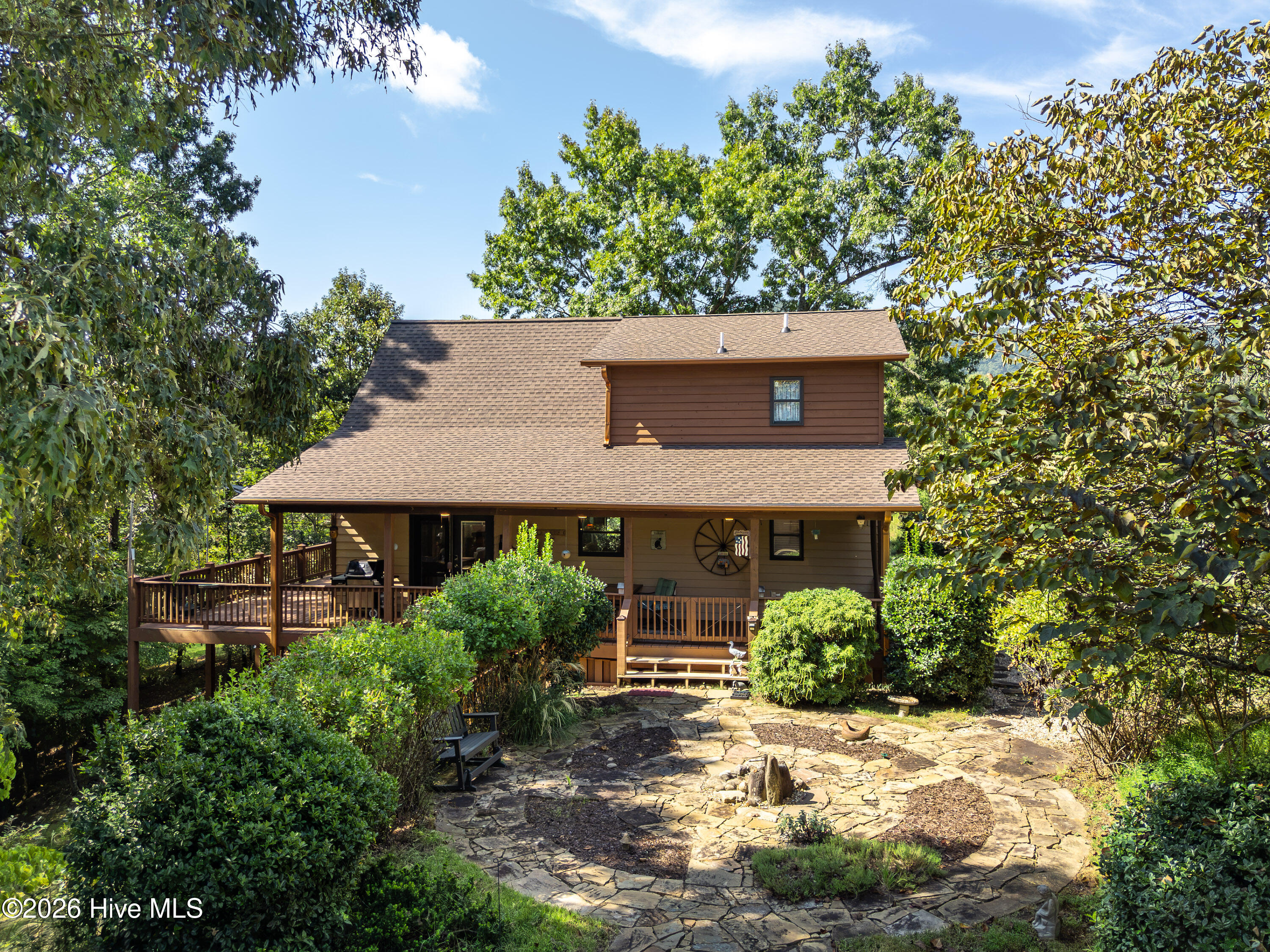 Brown two-story home with a covered porch, surrounded by trees and a curved stone patio.