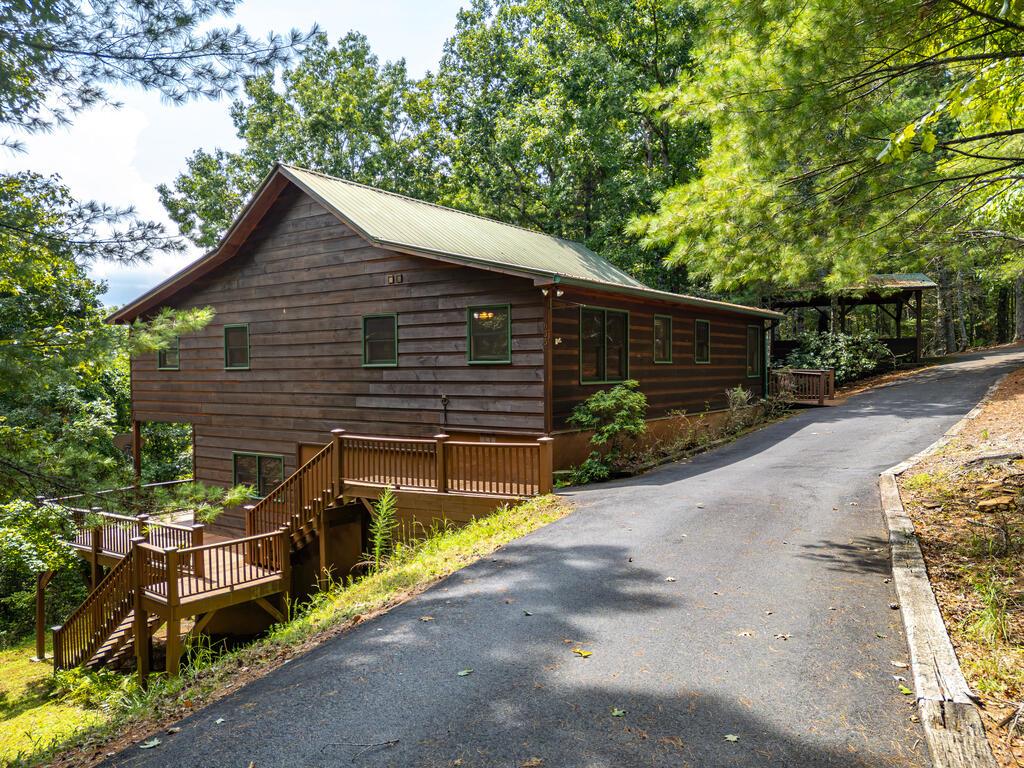 Wood-sided home in a wooded setting with a raised deck and uphill driveway.