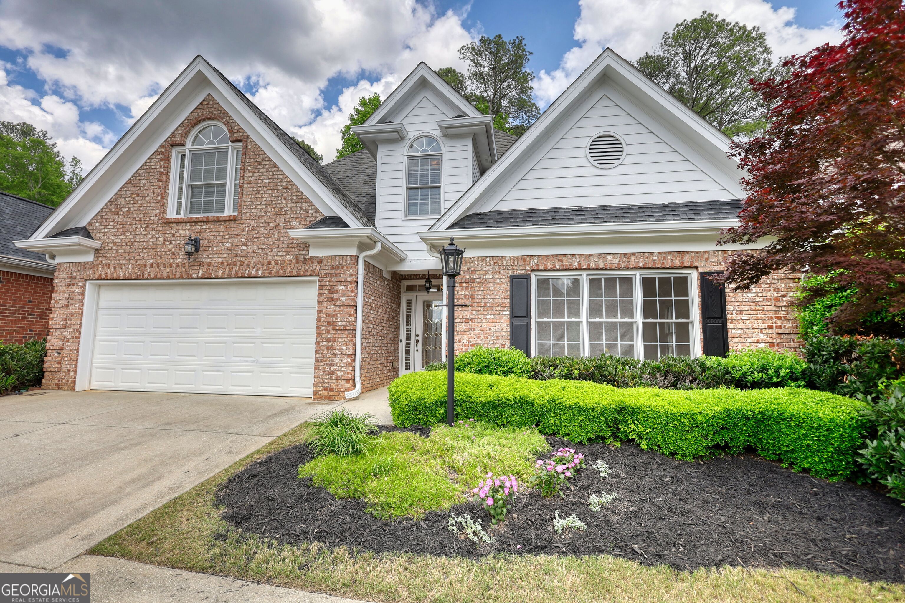 Two-story brick and white-sided home with a double garage and neatly landscaped front garden.